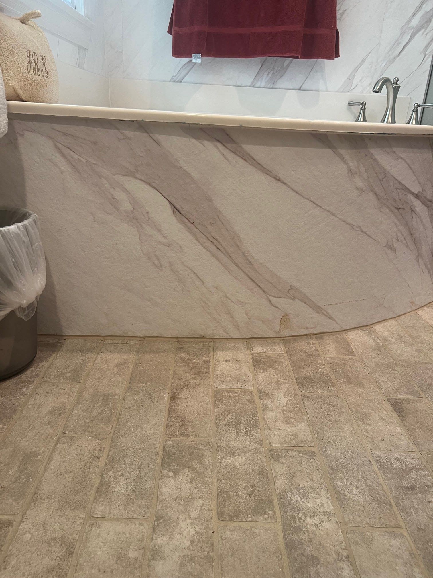 Bathroom with curved marble-look surround. Beige tile floor and red towel visible.