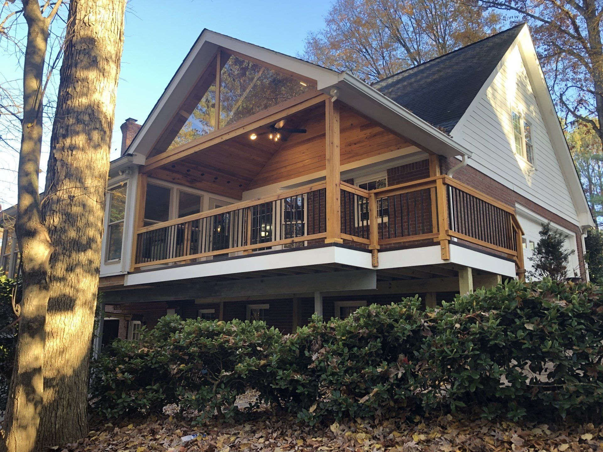 Wooden porch extension on a house, with a gabled roof and surrounding trees.