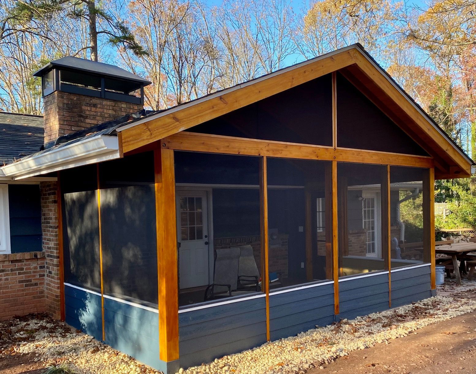 Screened-in porch with dark blue siding, stained wooden frame, and a brick chimney.