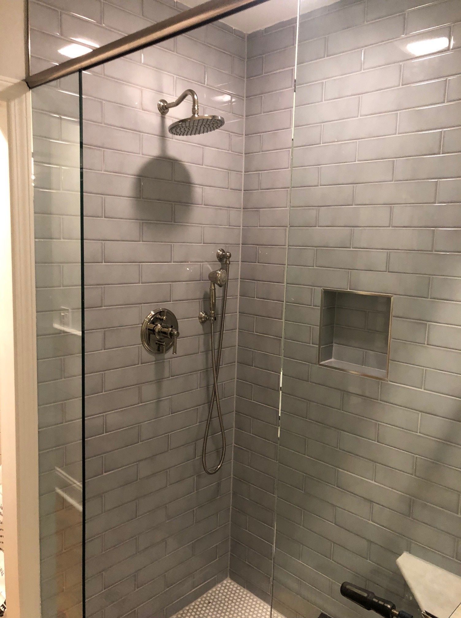Glass-walled shower with gray subway tile, silver fixtures, and a recessed shelf.