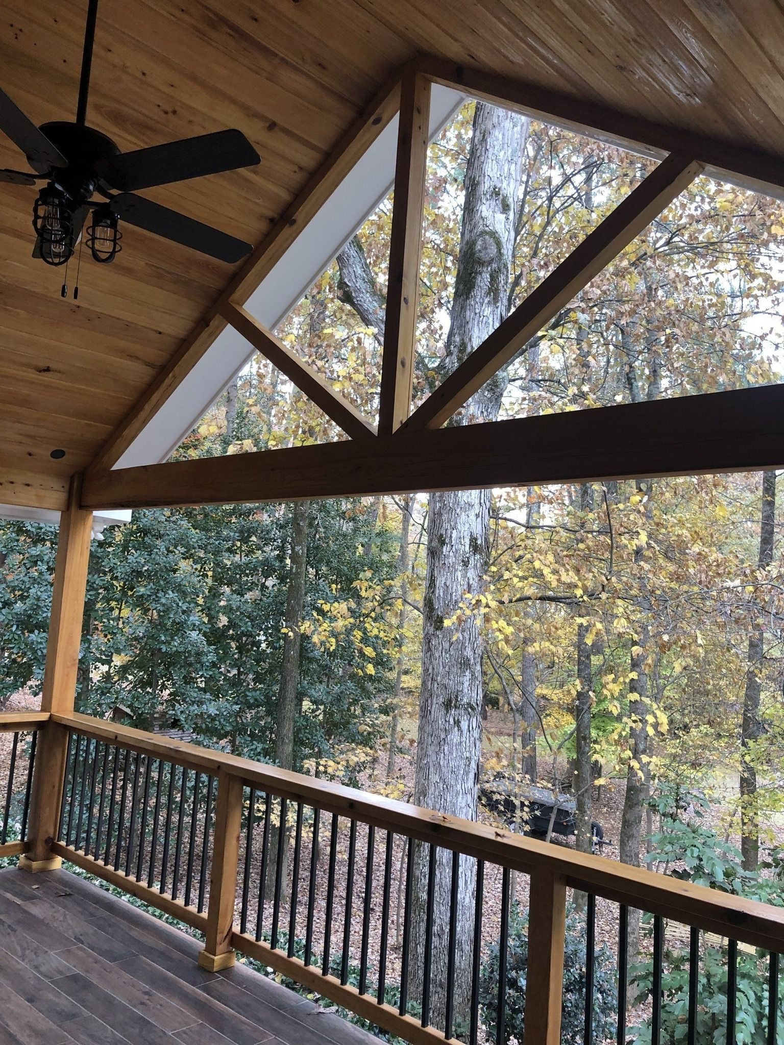 Wooden porch with dark railing and a triangular window looking out at a forest.