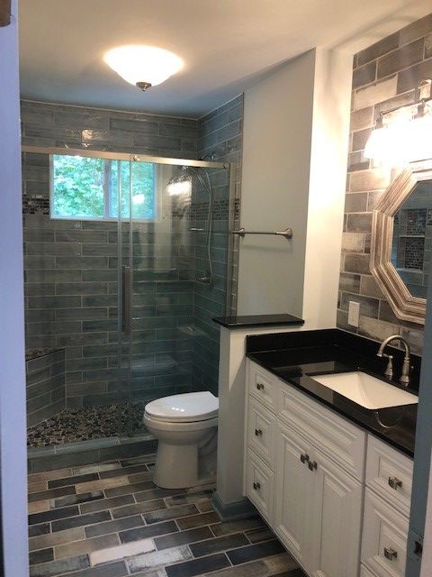 Bathroom with glass shower, white vanity, dark countertop, and decorative gray tile.