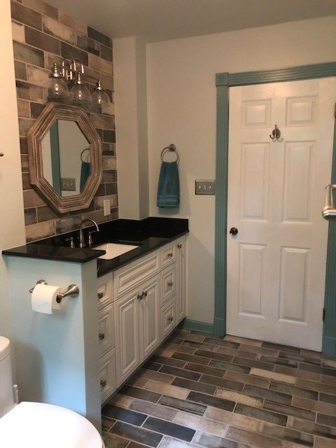 Bathroom with brick-style tile floor and wall. White vanity, black countertop, octagon mirror, and a door with teal trim.