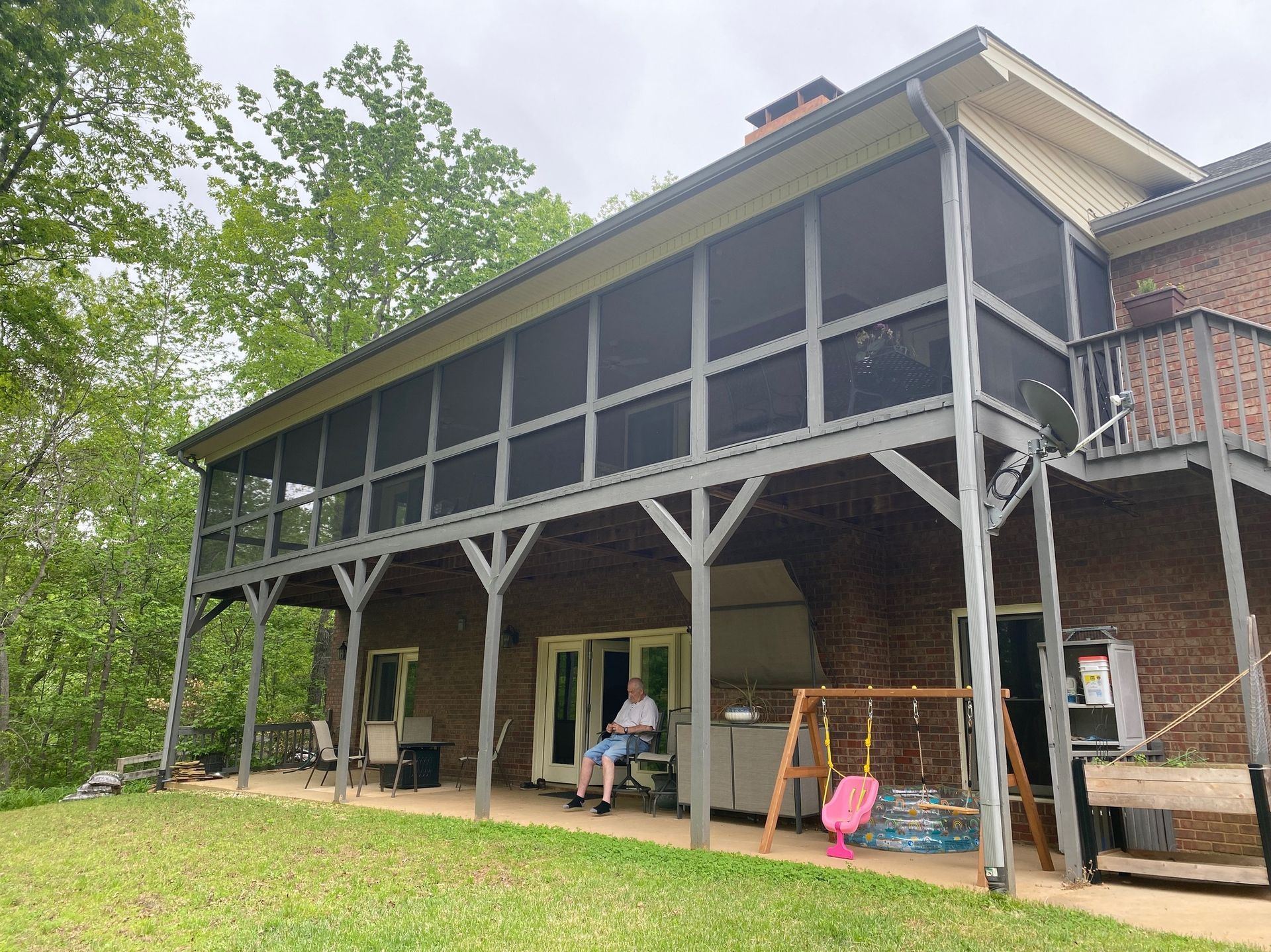 Screened-in porch on a brick house; person sits in a chair; swing set.