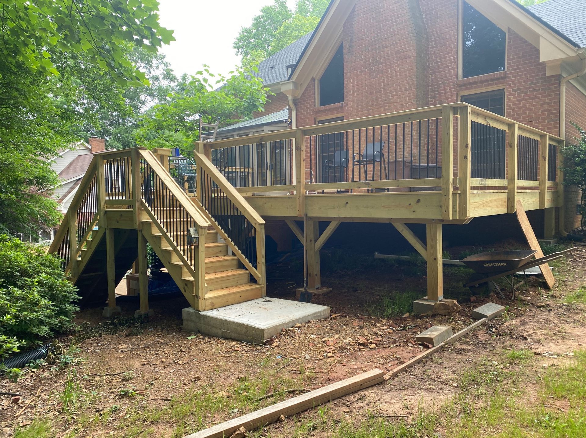 Wooden deck with stairs attached to a brick house. Railings have black metal balusters.