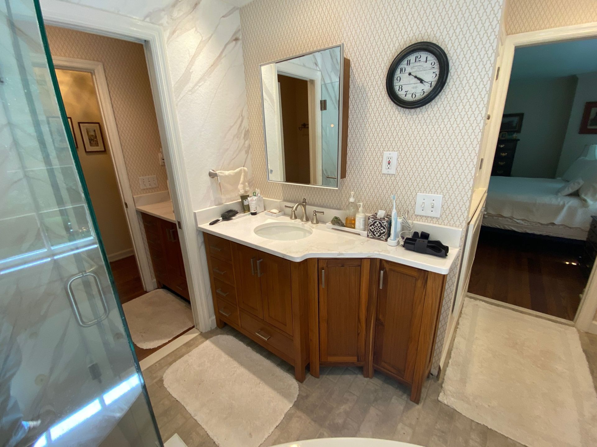 Bathroom with wooden vanity, mirror, clock, and doorway to a bedroom.