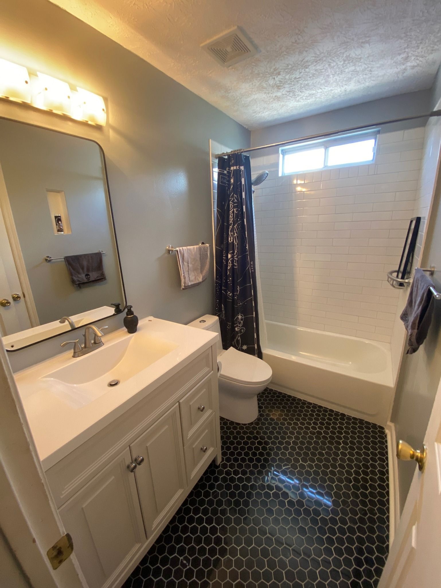 Bathroom with white vanity, black hexagon tile floor, white-tiled shower, blue walls, and a dark shower curtain.