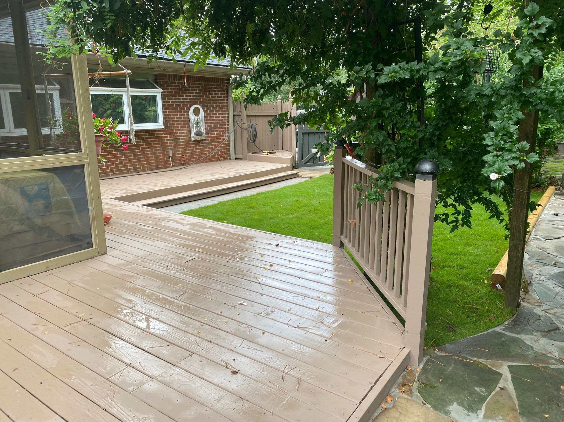 Deck overlooking a lawn, next to a brick building. Wooden railing and tree on the right.