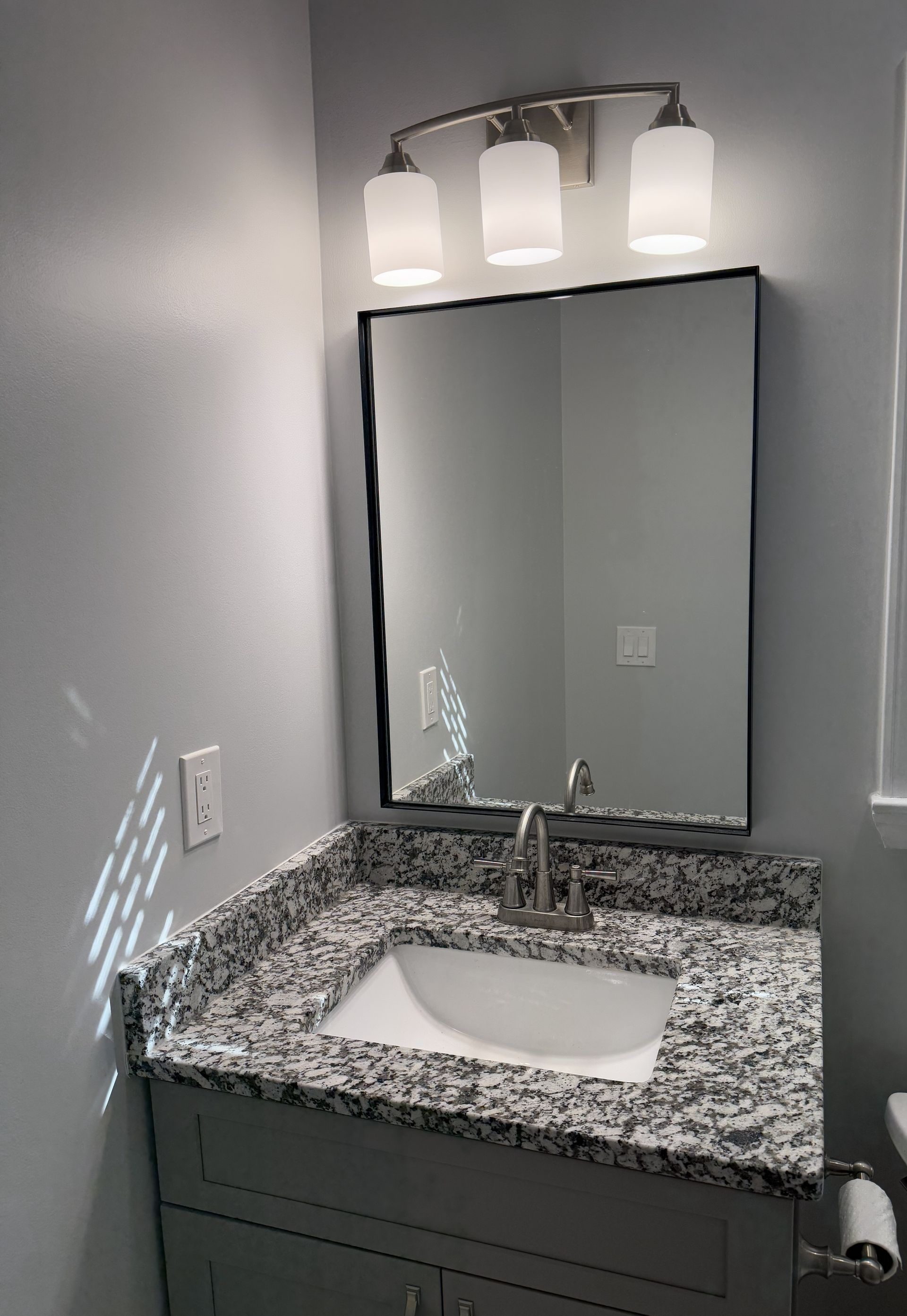 Bathroom with gray vanity, granite countertop, mirror, three-light fixture, and sink.