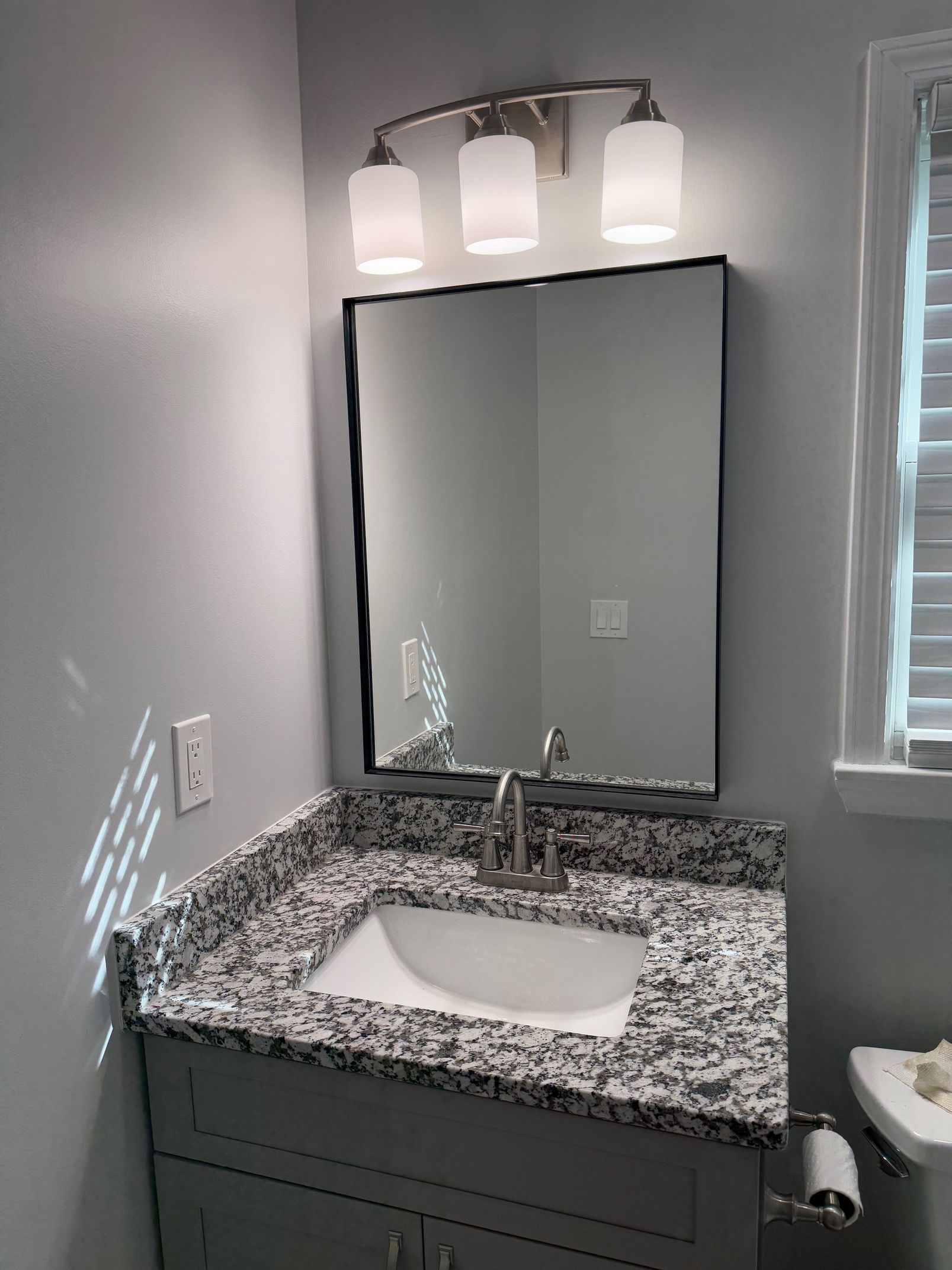 Bathroom with gray vanity, granite countertop, mirror, and three-light fixture above the sink.