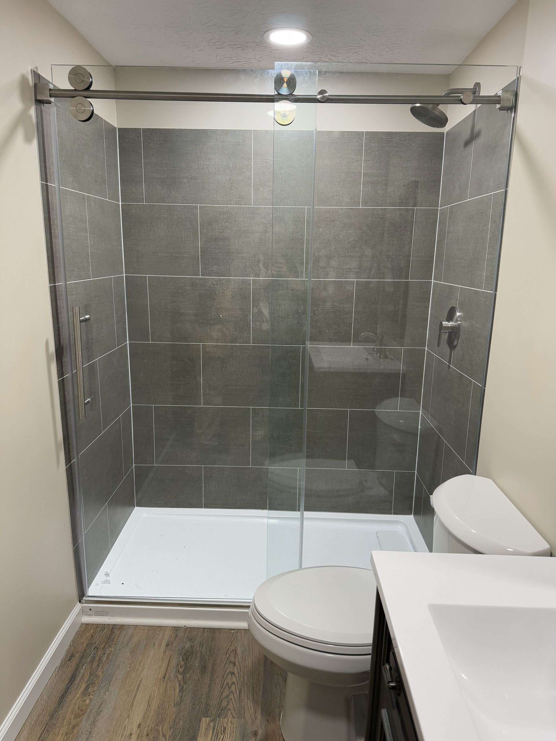 Bathroom with a gray tiled shower, toilet, and a white vanity with a sink.