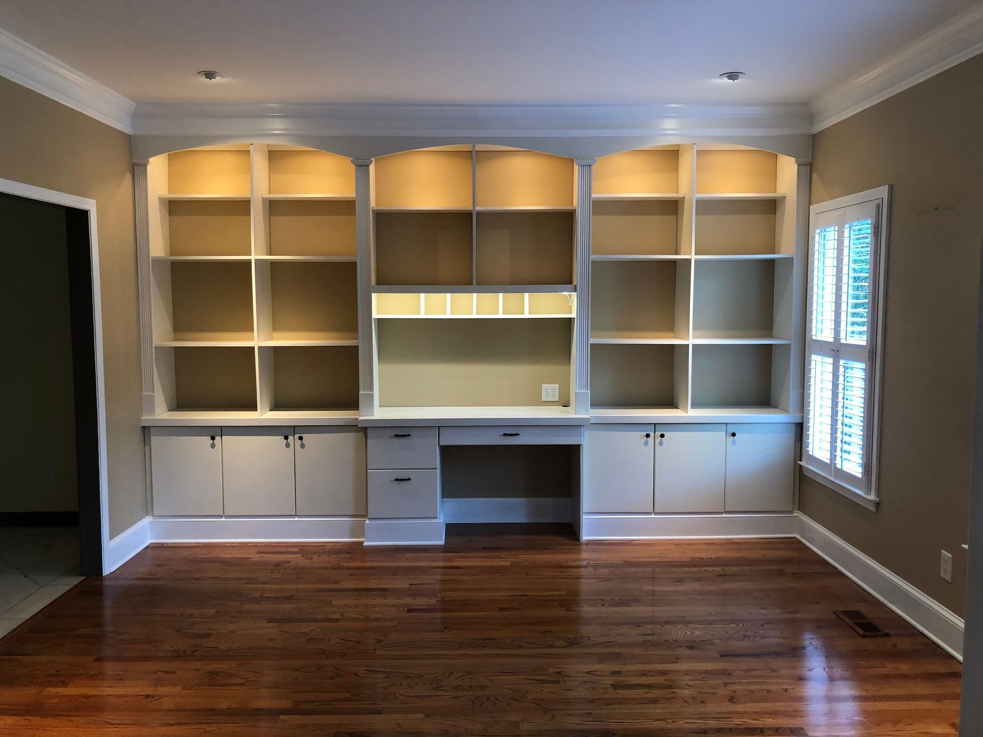 Built-in white bookshelves and desk in a room with hardwood floors and a window.