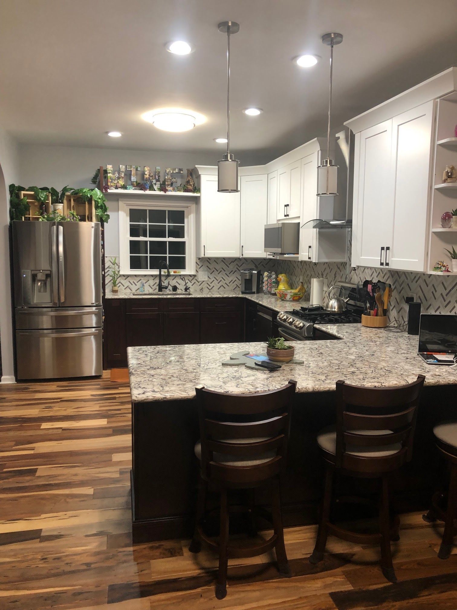 Kitchen with stainless steel appliances, white cabinets, dark island with granite countertop, wooden floor.