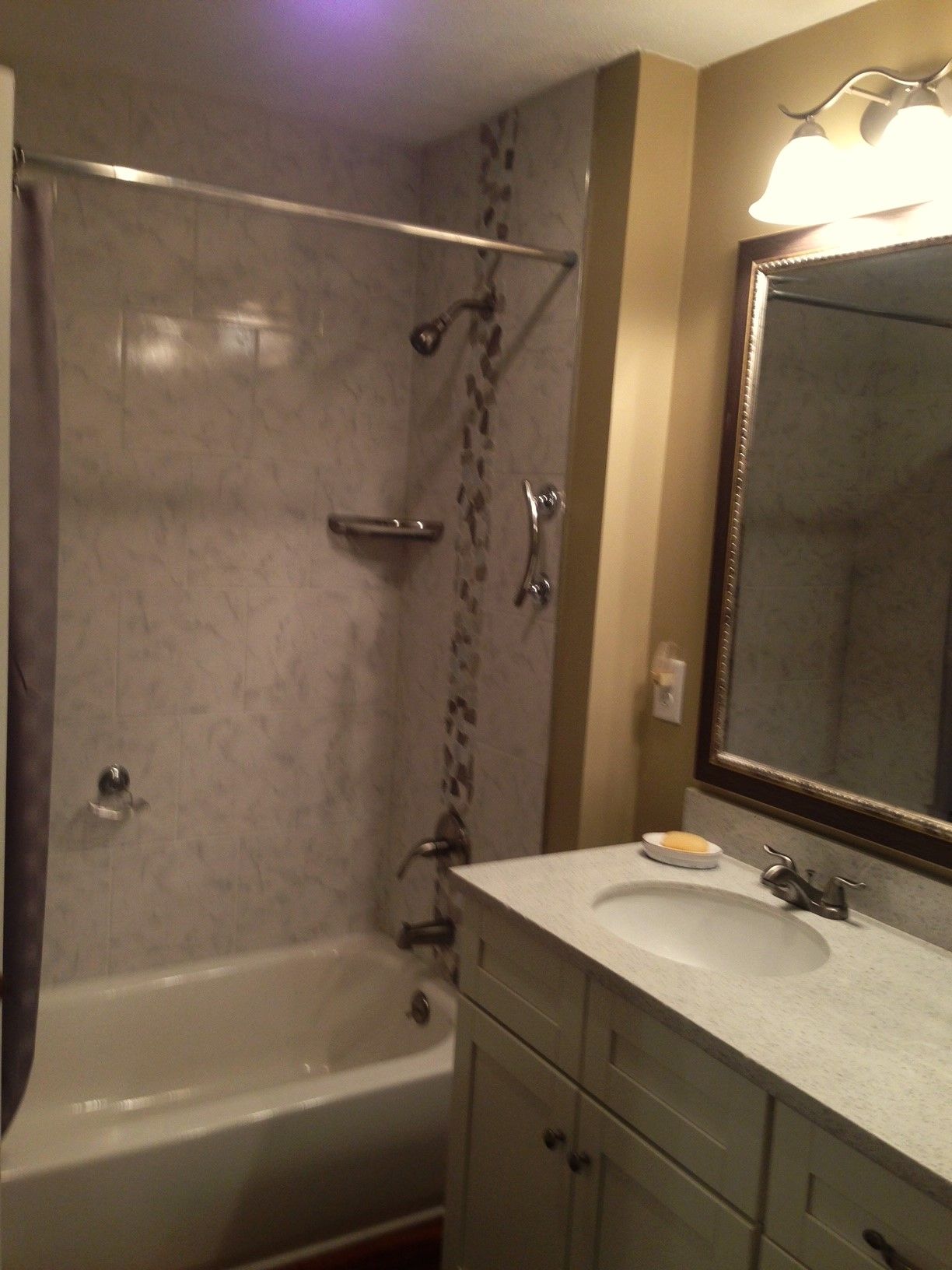 Bathroom with a white tub, marble tile, and a vanity with a mirror.