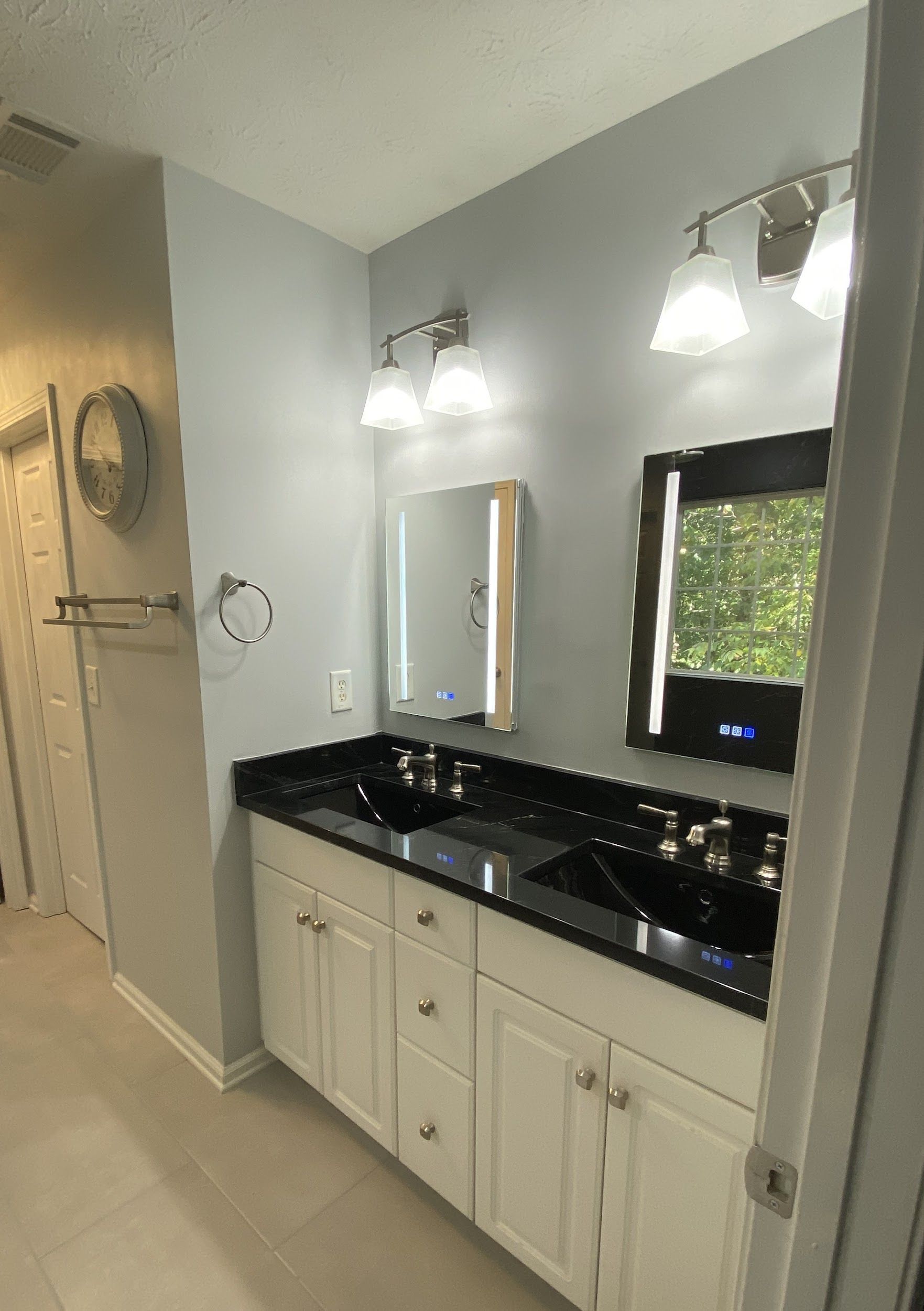 Bathroom with white vanity, black countertop and sinks, mirrors, and sconces.