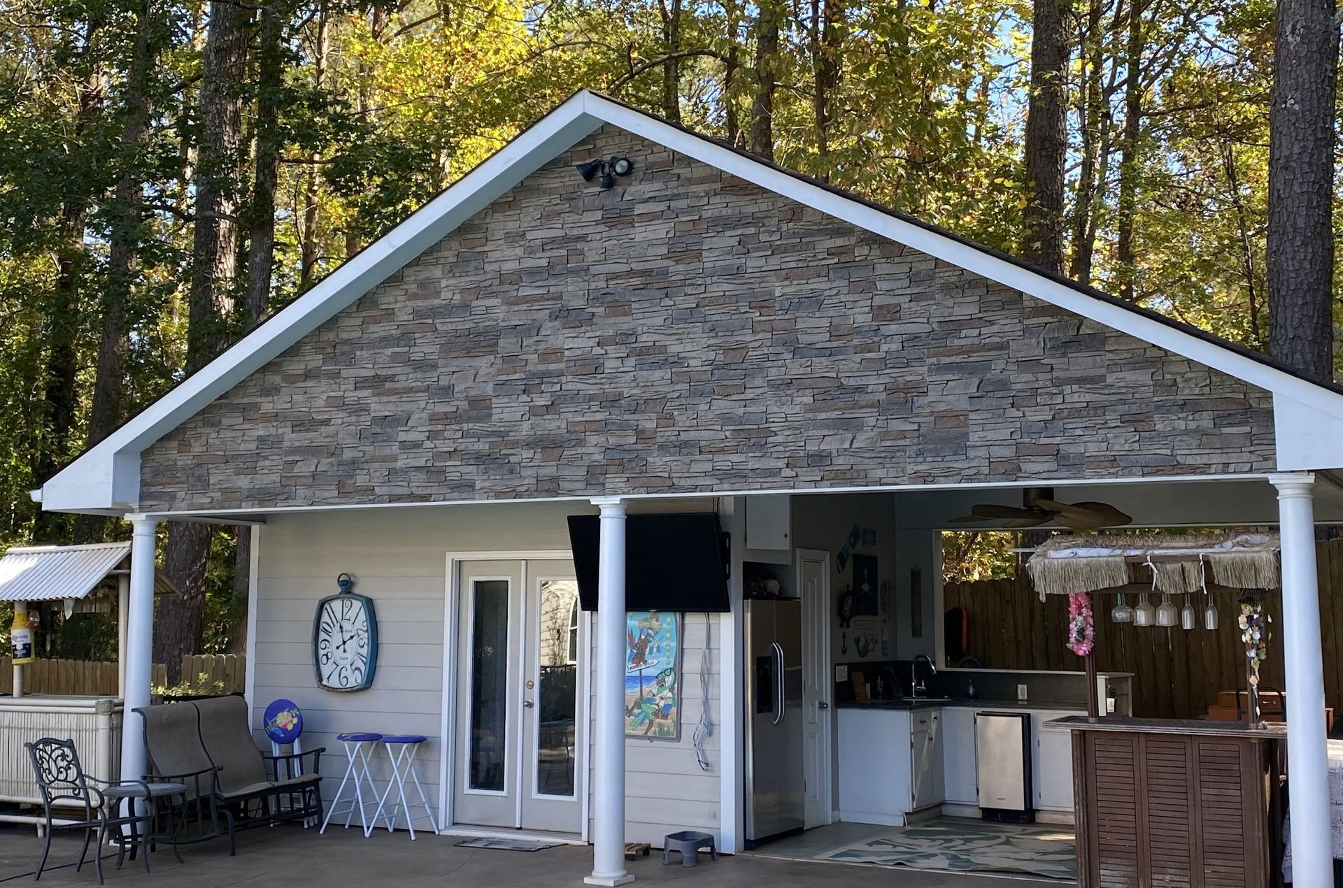 Outdoor kitchen with a stone-covered gable. Includes a refrigerator, TV, and seating area.