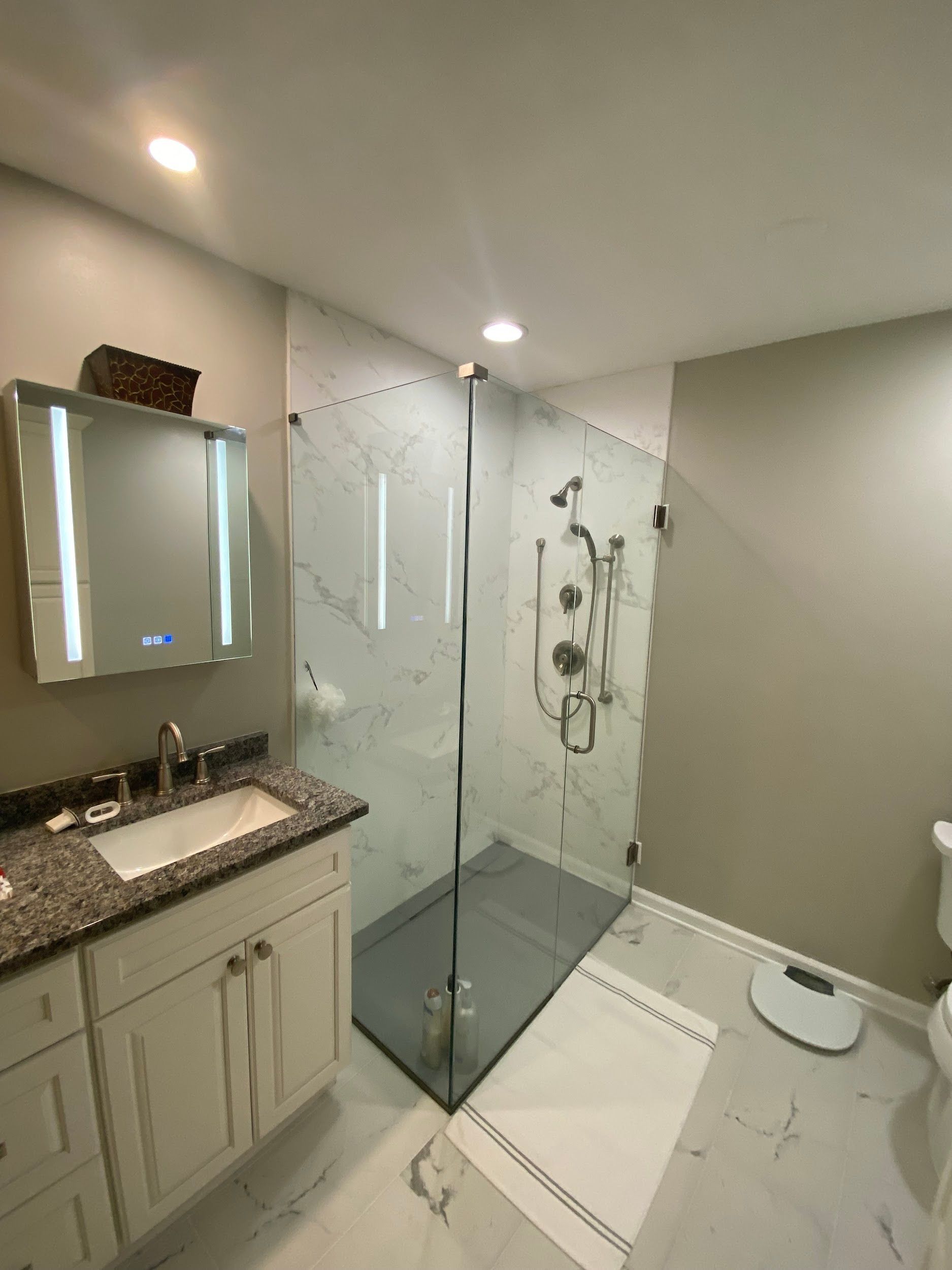 Modern bathroom with a glass shower, marble tile, and a white vanity.