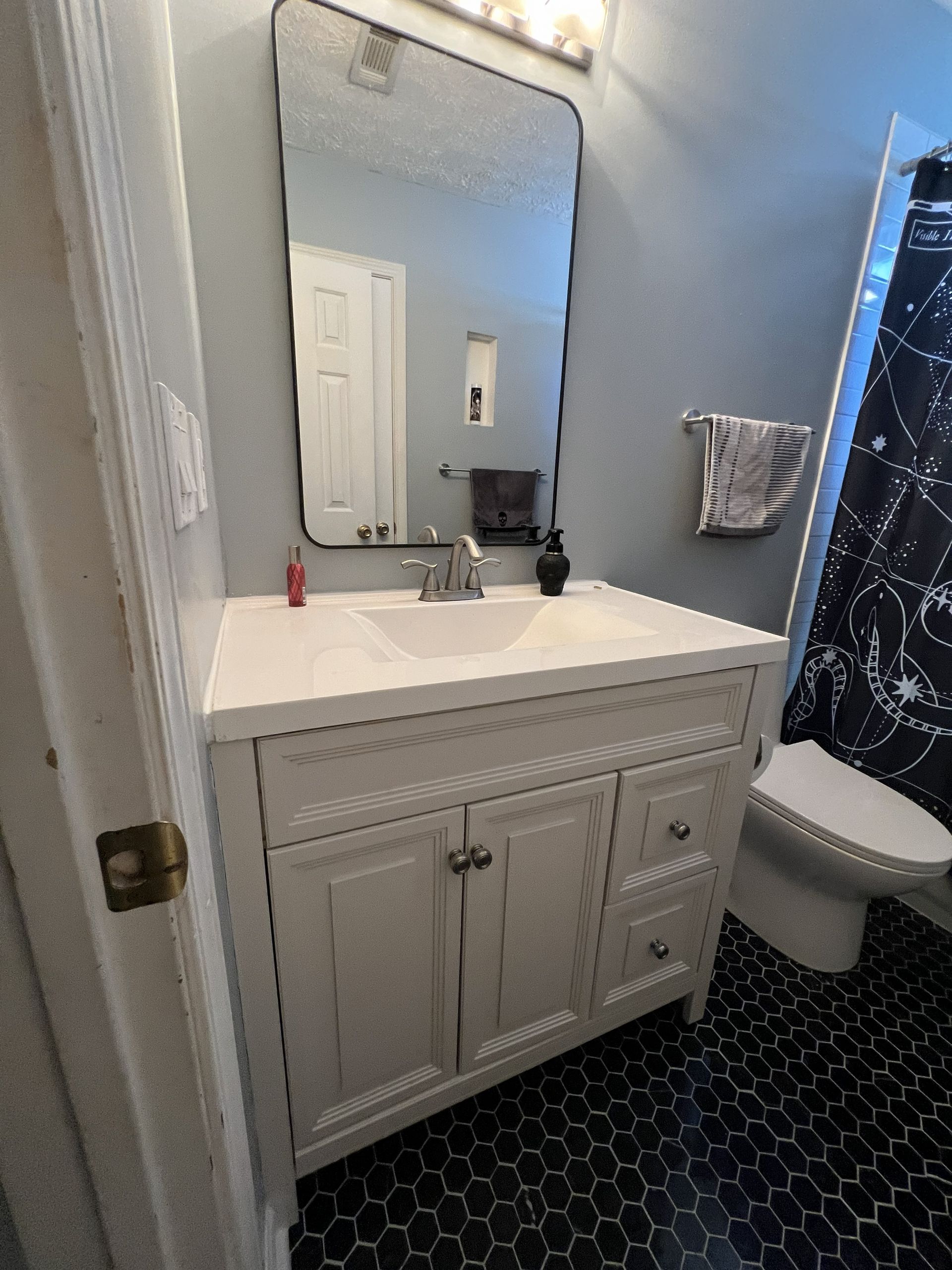 White bathroom vanity with sink and mirror, blue wall, black tile floor, and a toilet.