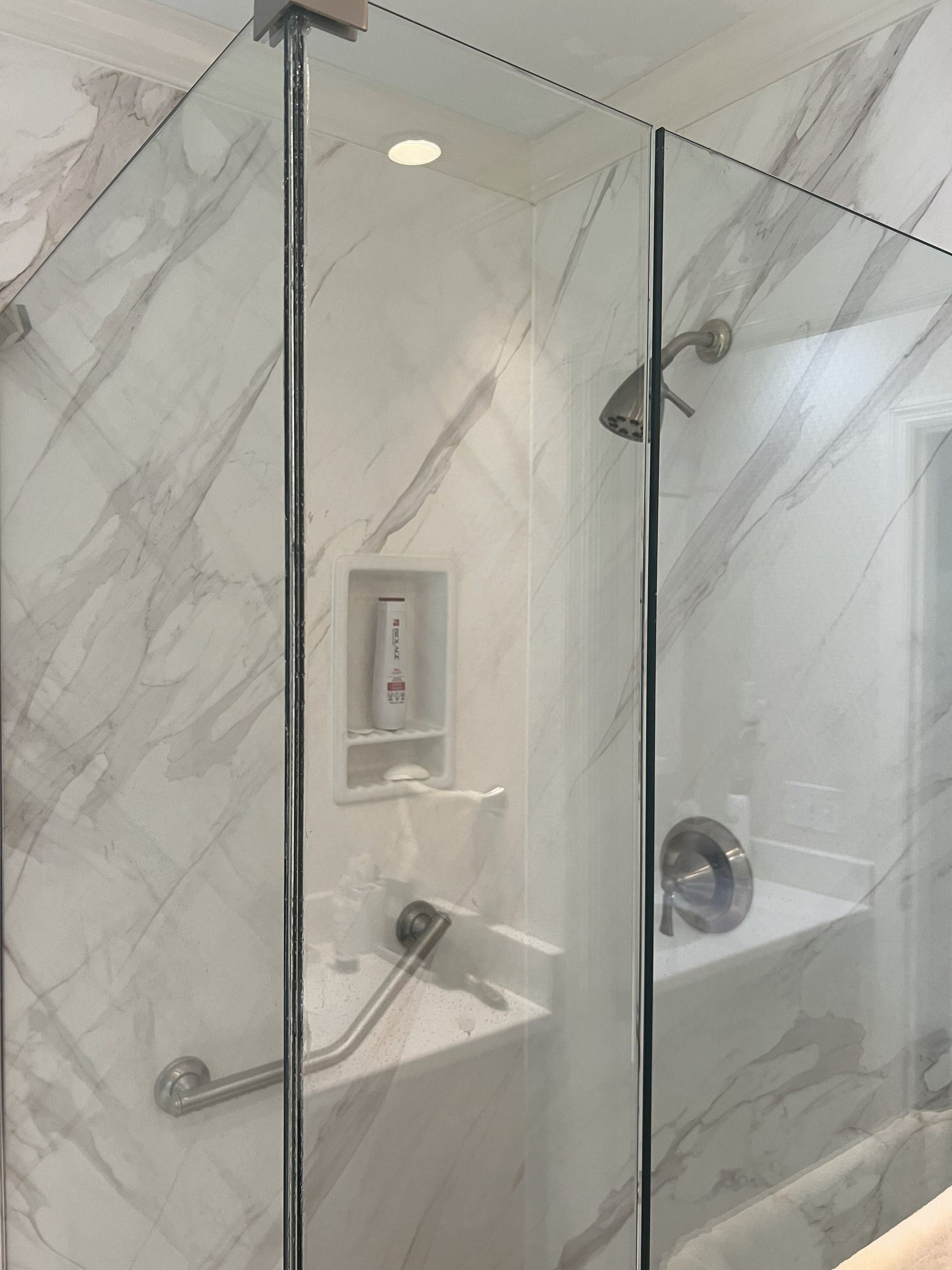 Shower with marble-look walls, glass doors, built-in shelf, and grab bars.