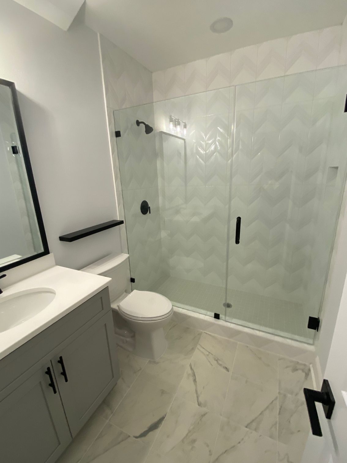 Modern bathroom with a glass shower, gray vanity, and white toilet.