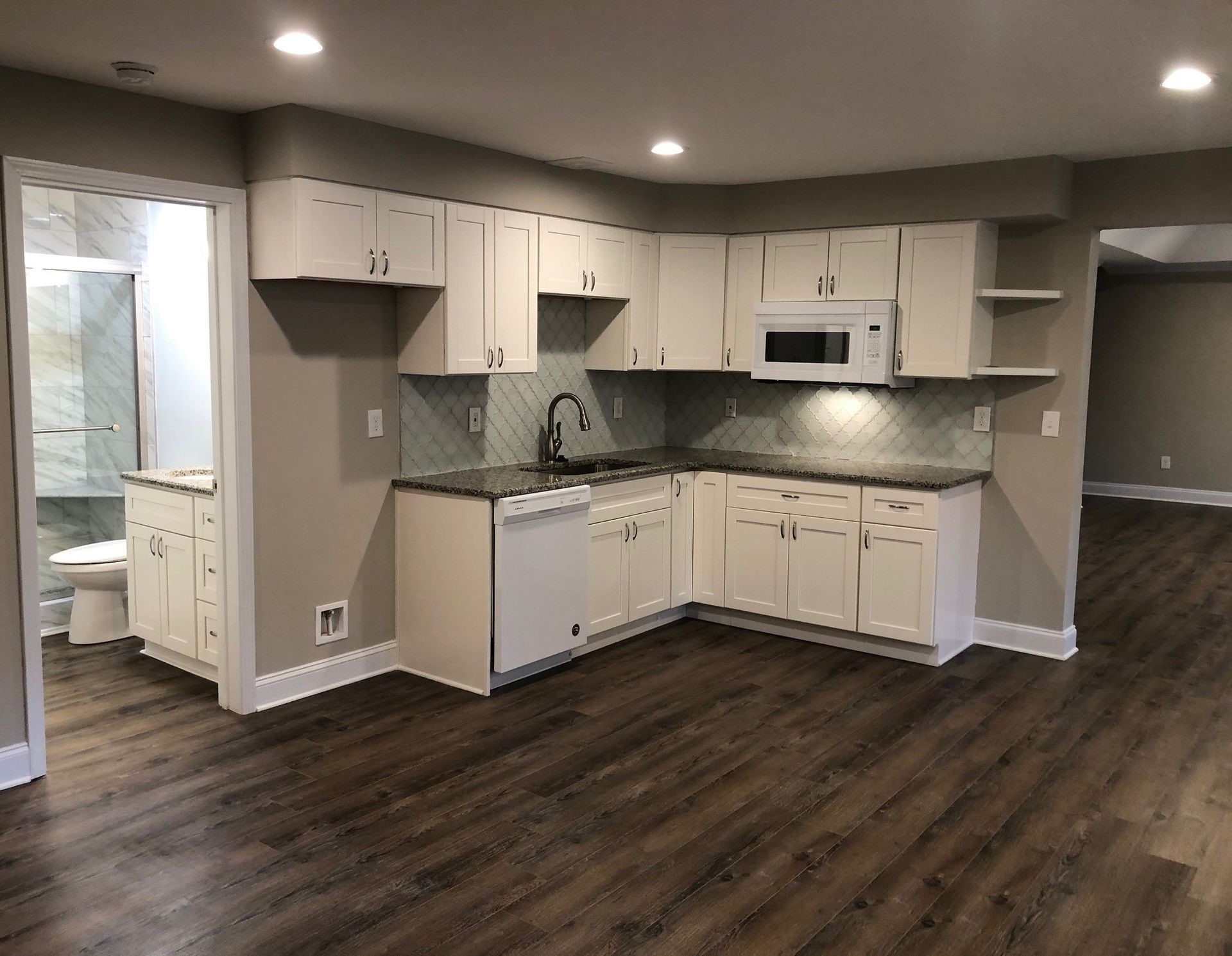 White kitchen with a dishwasher, microwave, and sink, next to a bathroom with a toilet and sink.