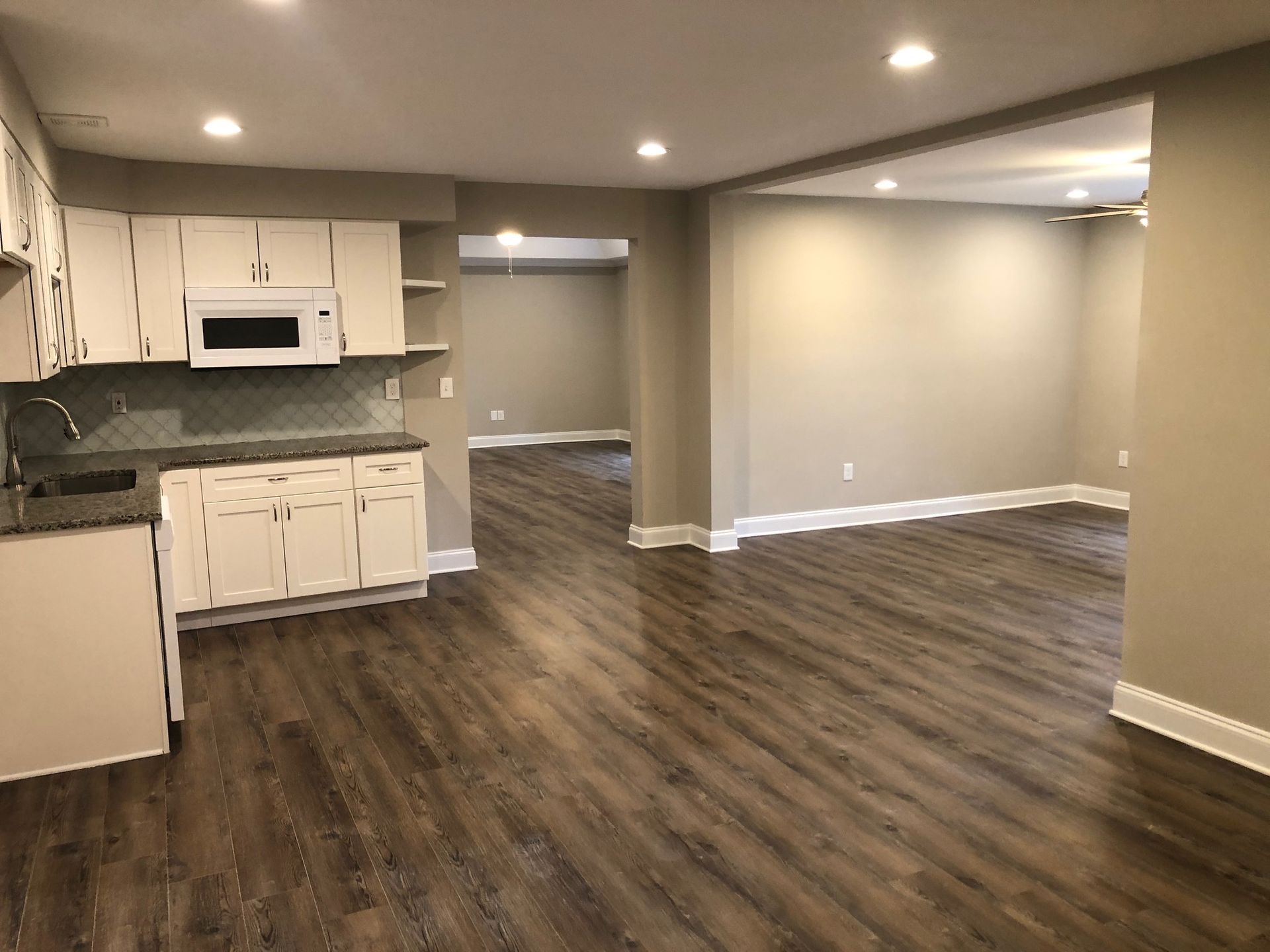Interior view of a remodeled living space with white cabinets, dark wood-look flooring, and neutral walls.