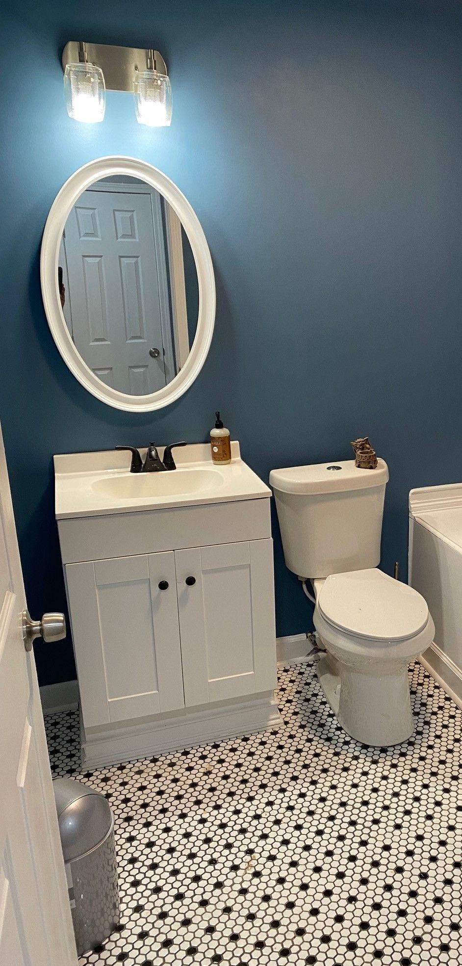 Bathroom with white vanity, oval mirror, blue walls, and patterned floor.