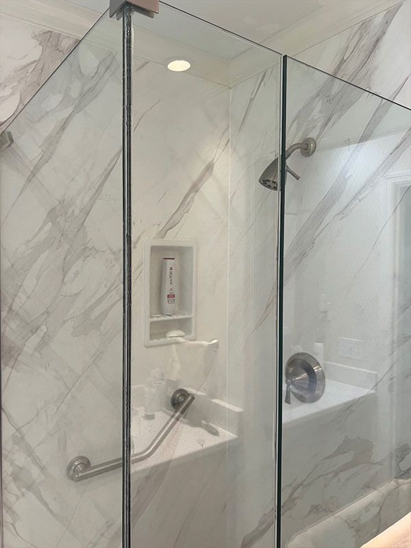 Glass shower enclosure with white marble-look walls, a built-in bench, and a showerhead.