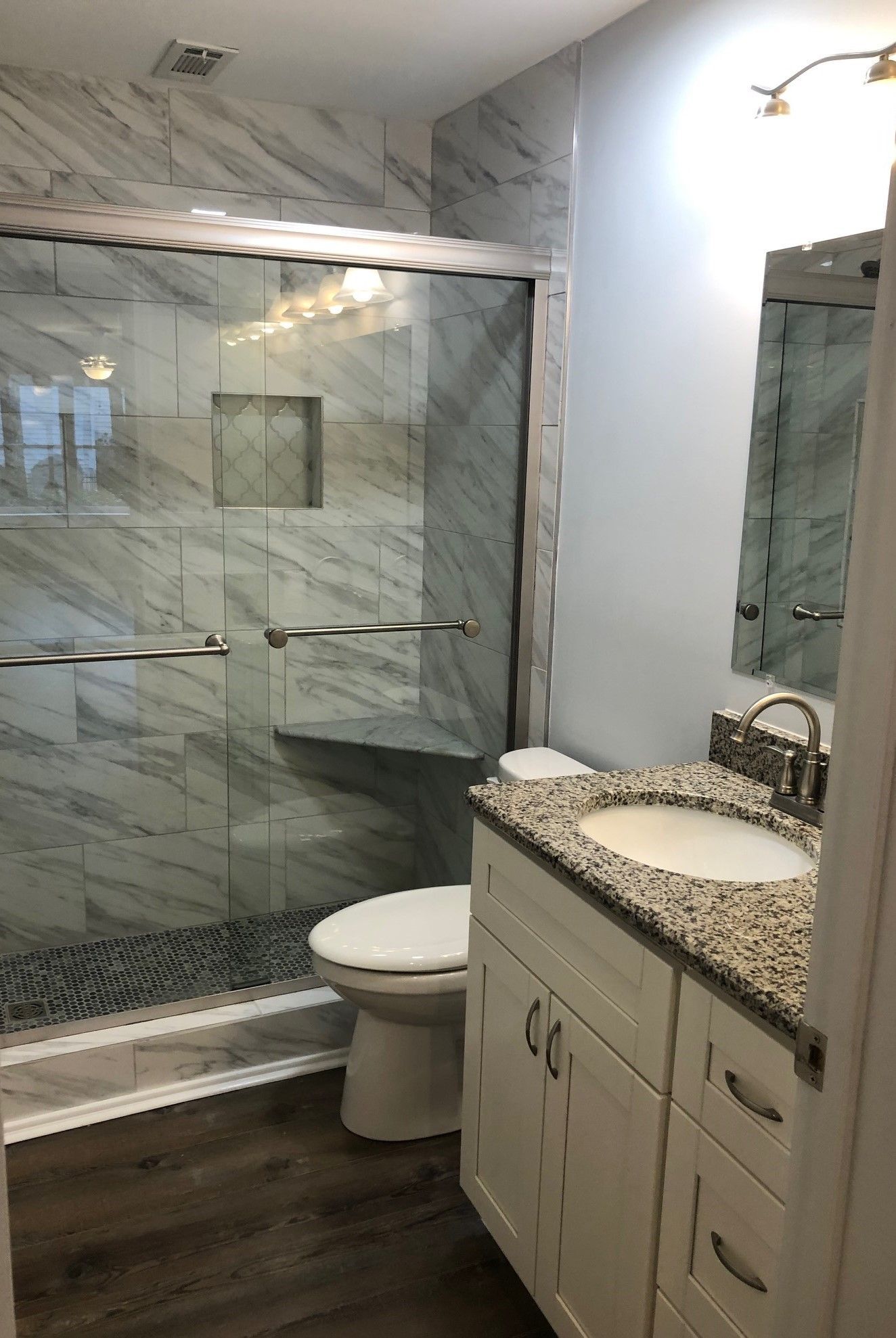 Bathroom with marble-look tile, glass shower, white vanity with granite countertop, and wood-look flooring.
