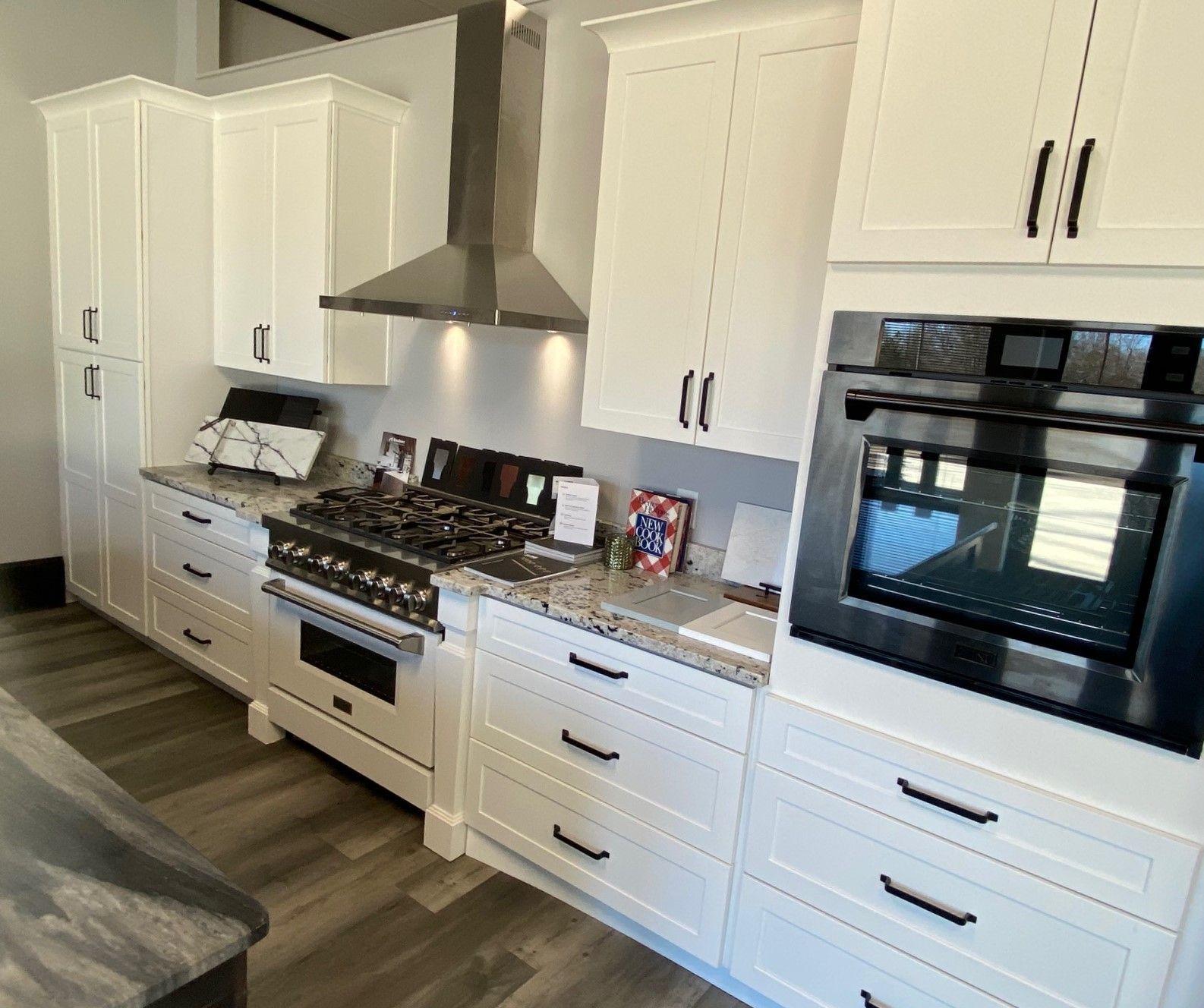 White kitchen with cabinetry, stainless steel range hood, oven, and granite countertops.