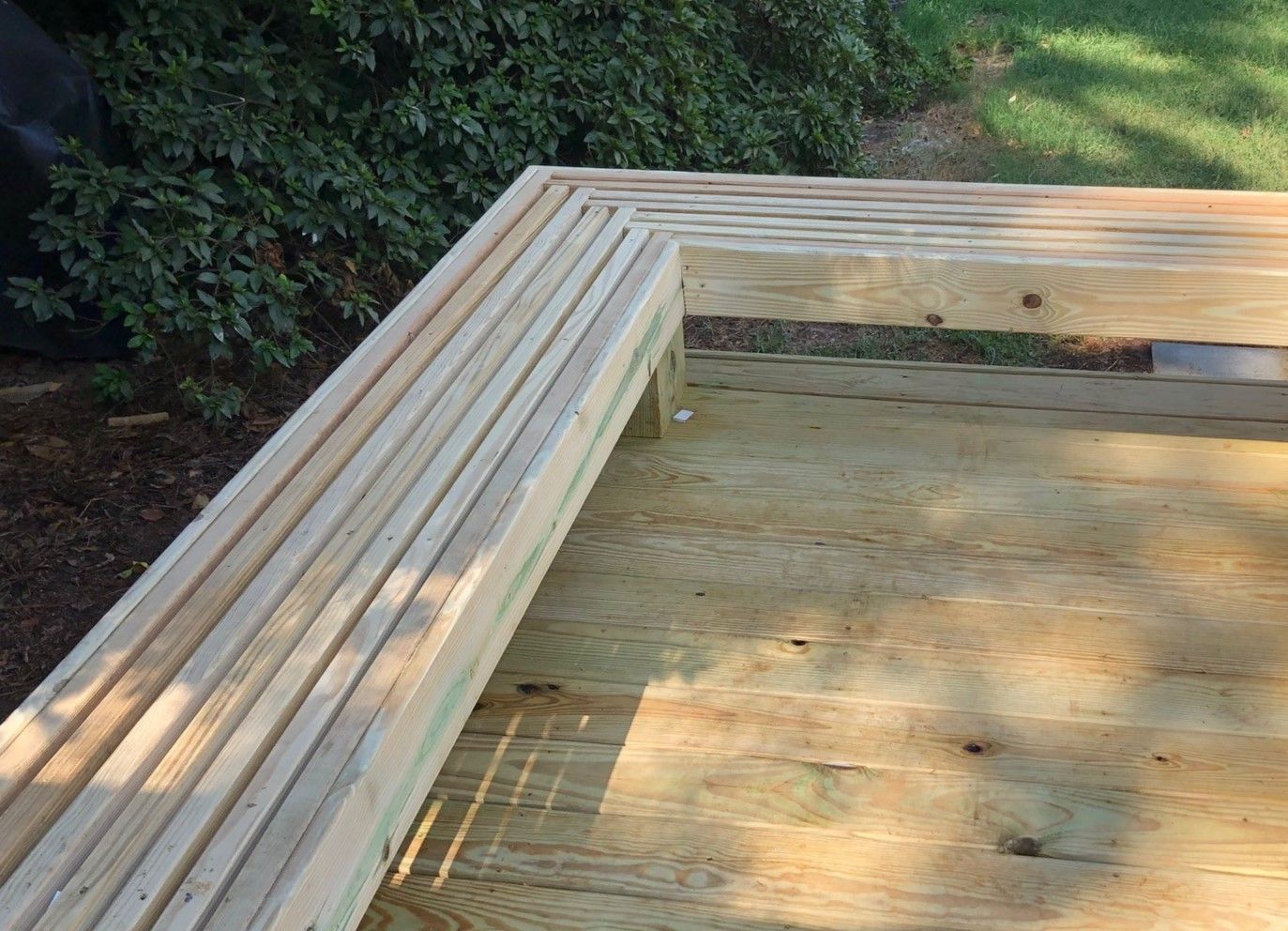 Wooden deck with a grooved railing and surrounding green foliage.