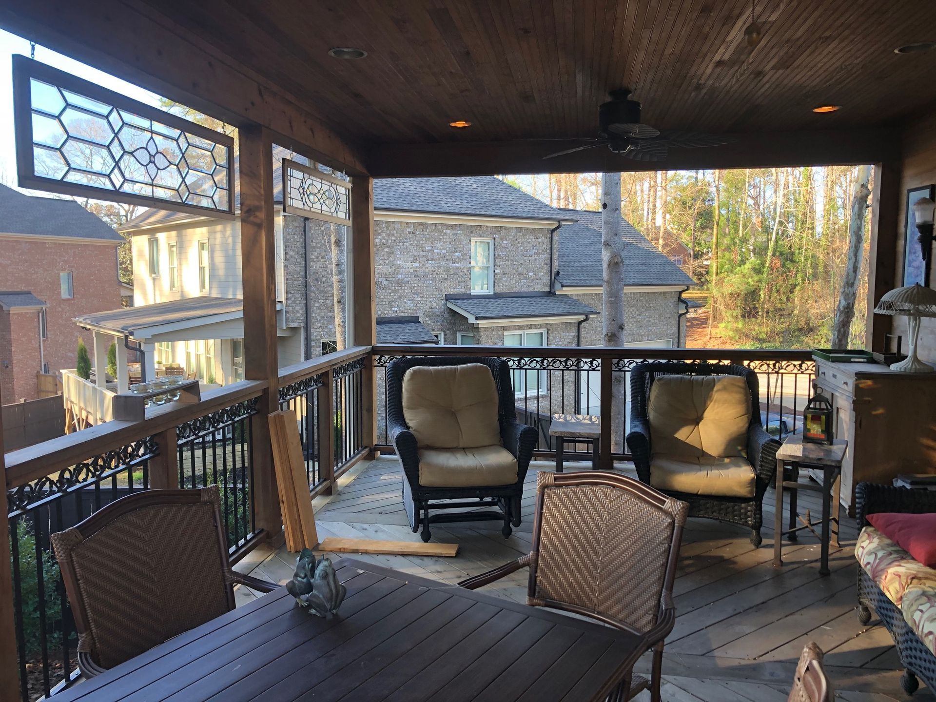 Covered porch with seating, table, and decorative railing, overlooking a neighborhood.