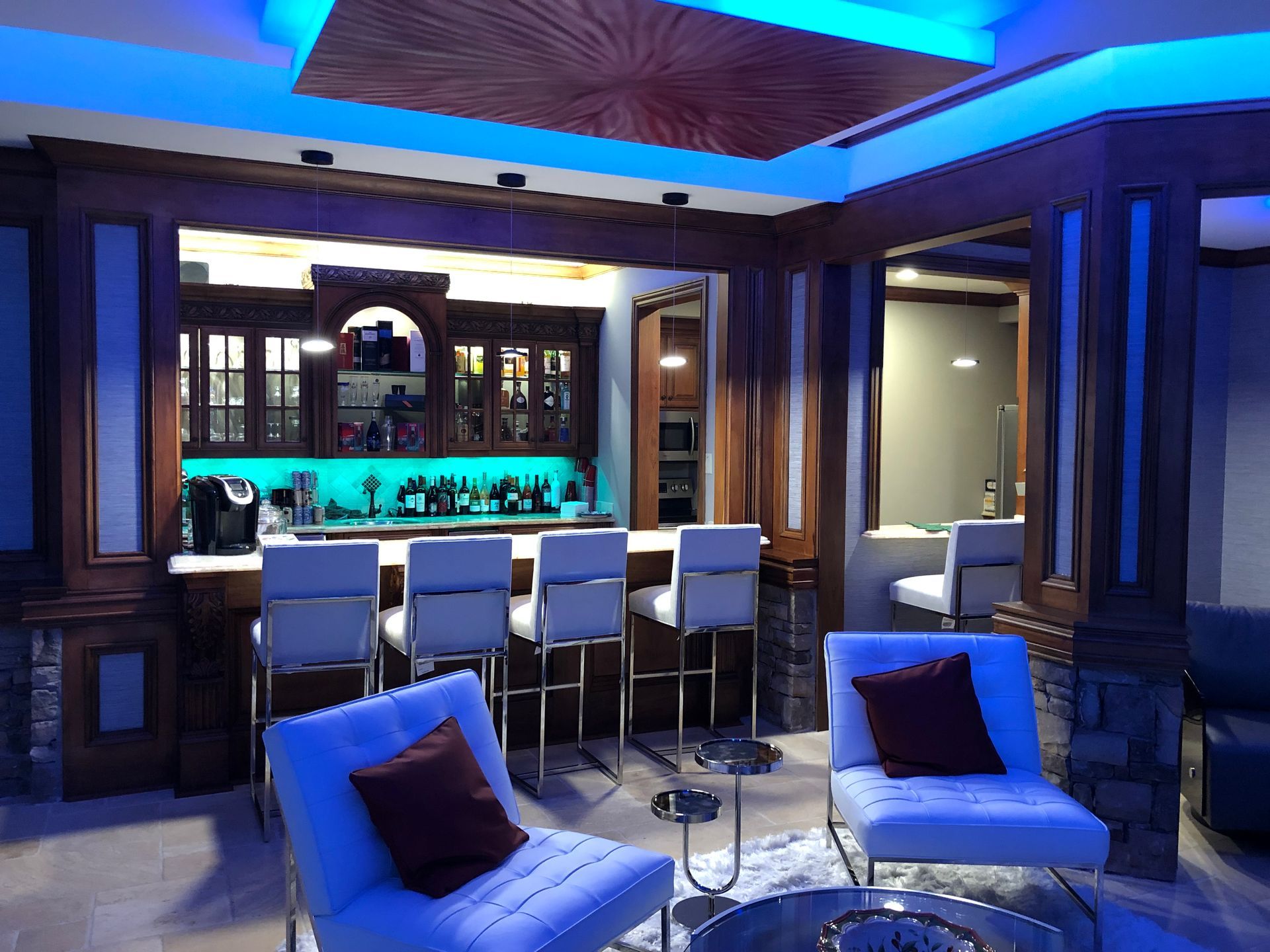 A luxurious home bar with blue lighting, seating, and a wood and stone design.