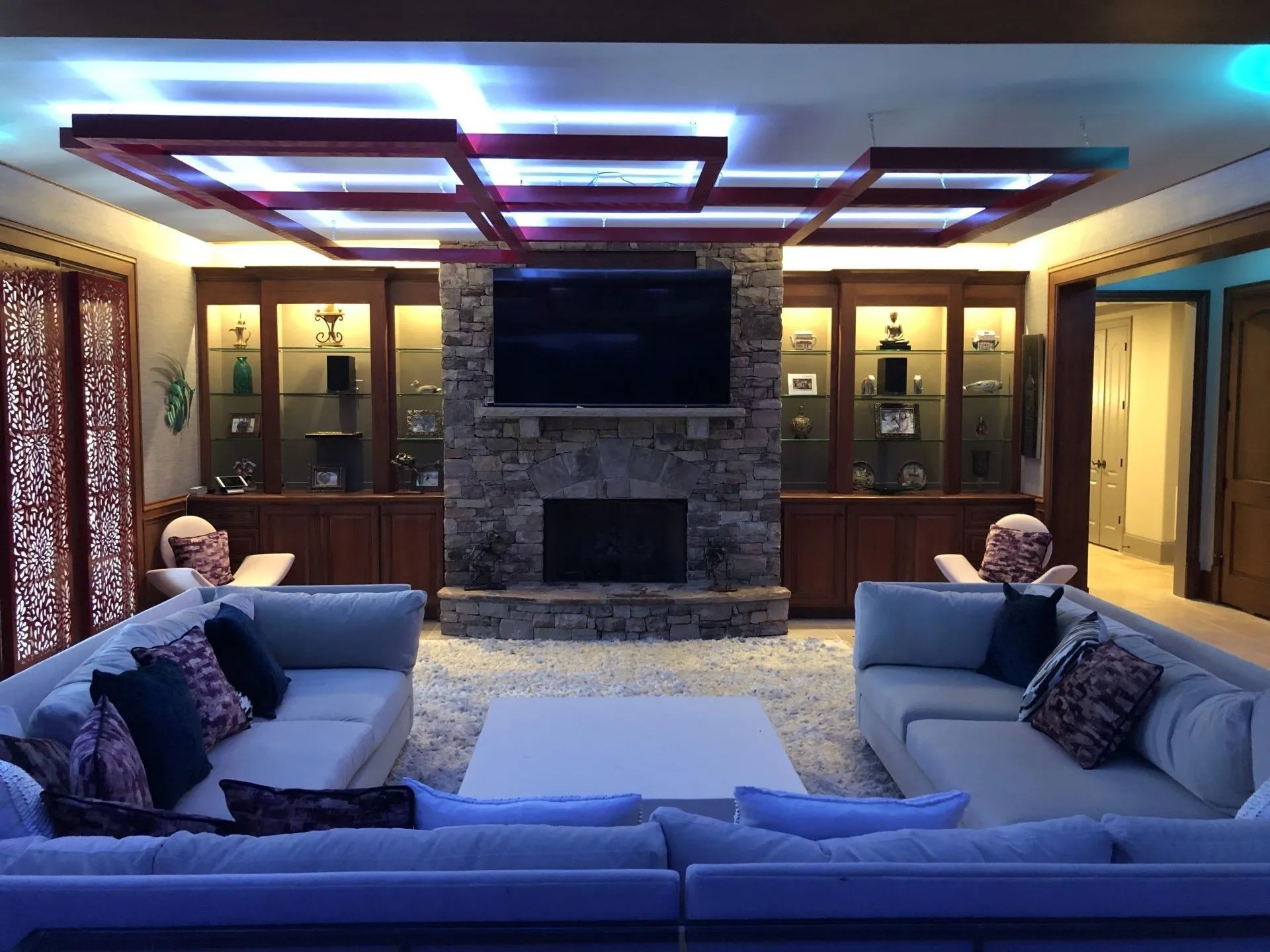Living room with stone fireplace, built-in cabinets, sofas, and recessed lighting in a grid pattern.