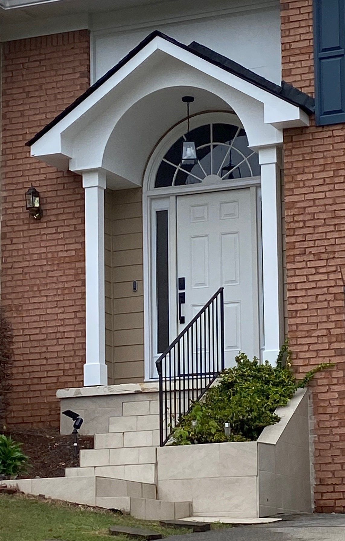 White front door with arched transom, brick facade, covered porch, steps, and railing.