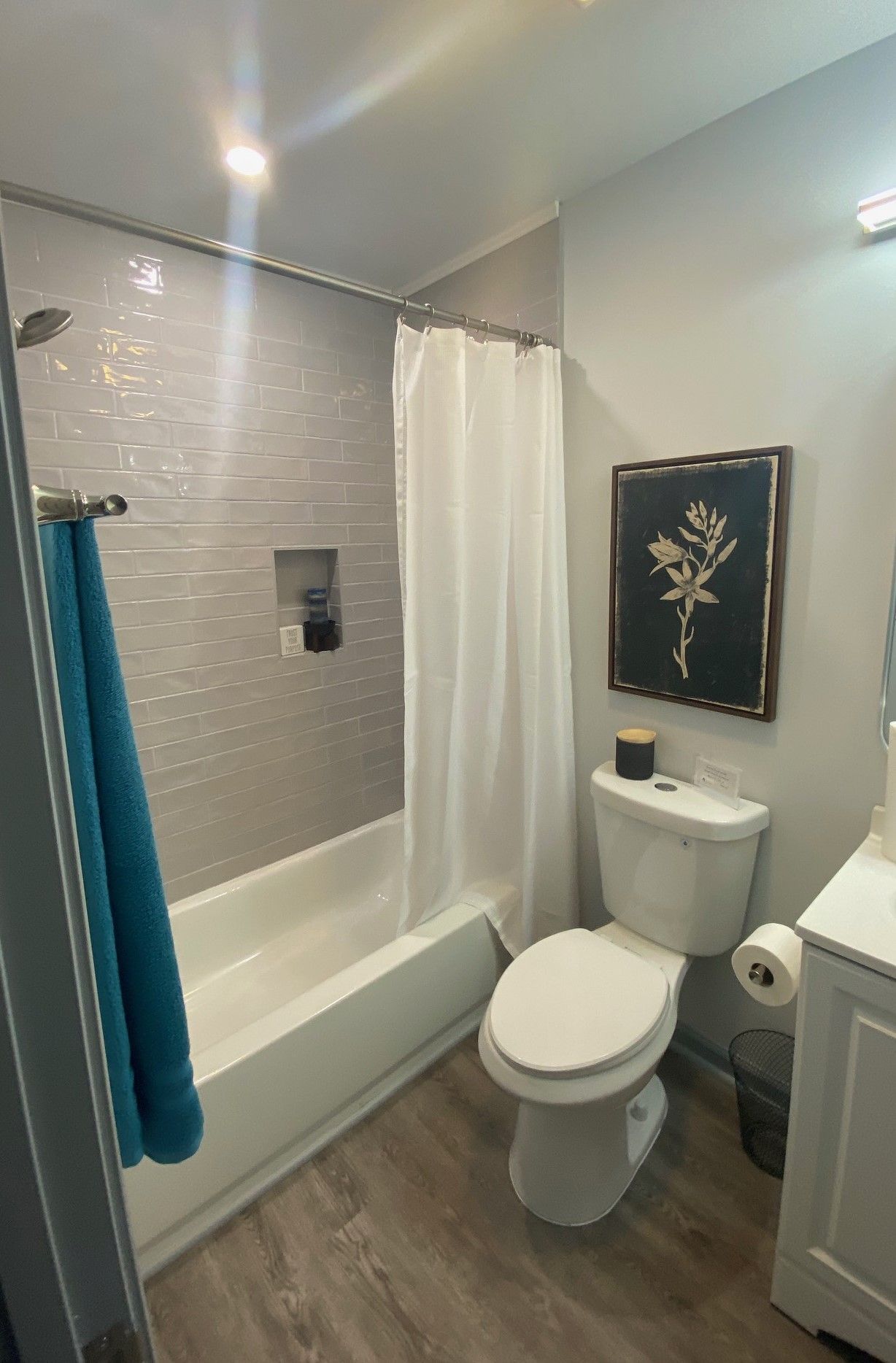 Bathroom with a bathtub, shower, toilet, sink, artwork, and gray and white decor. Blue towel.