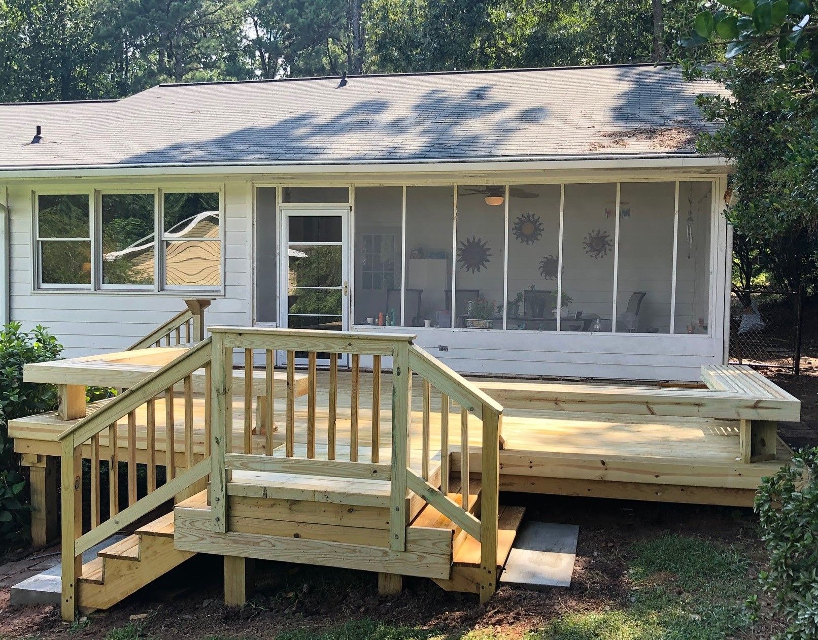 Newly built wooden deck with stairs in front of a house with a screened porch.