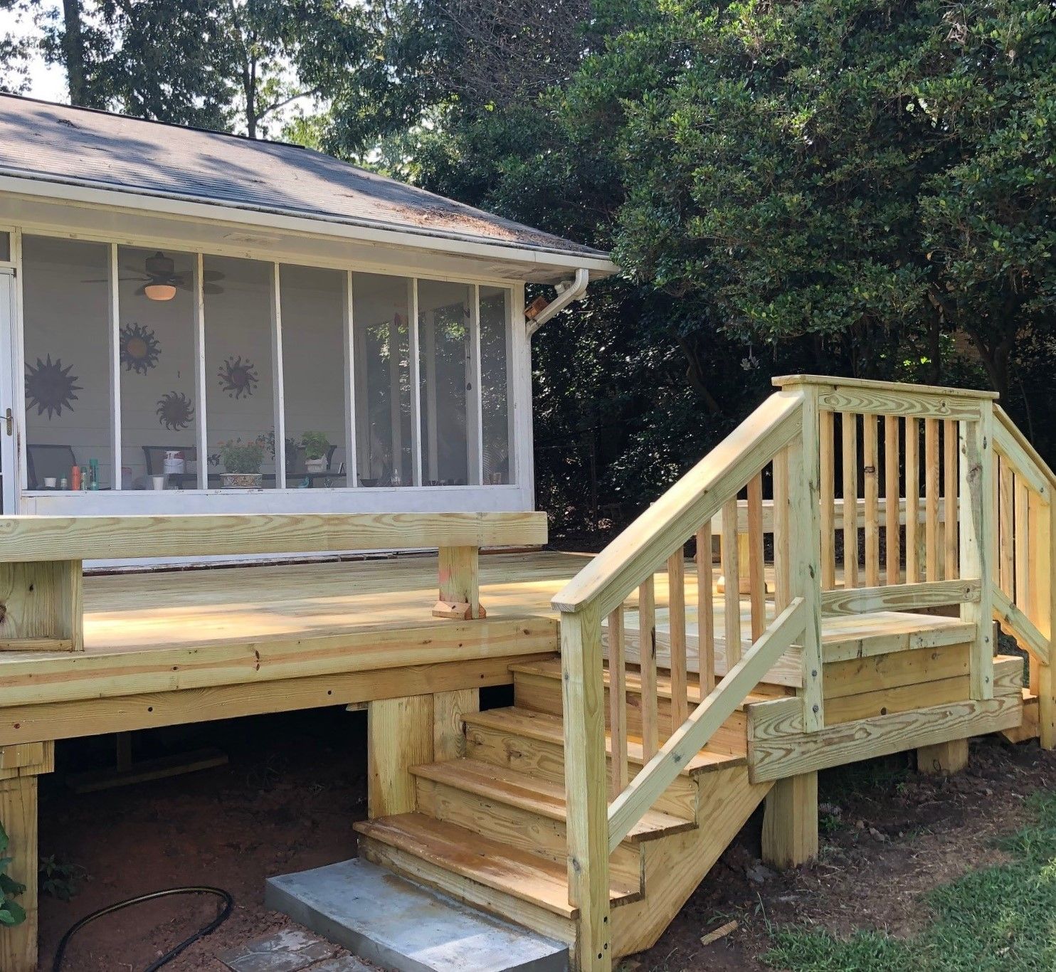 Wooden deck with stairs leading to a screened porch; surrounded by trees.
