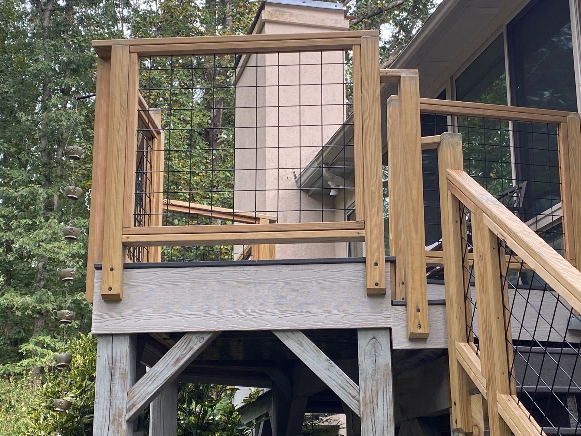 Wooden deck with railing. Black wire mesh infill. Building and trees in the background.