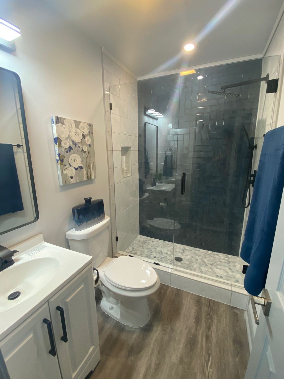 Bathroom with white vanity, toilet, and a glass-enclosed shower with dark gray tiles.