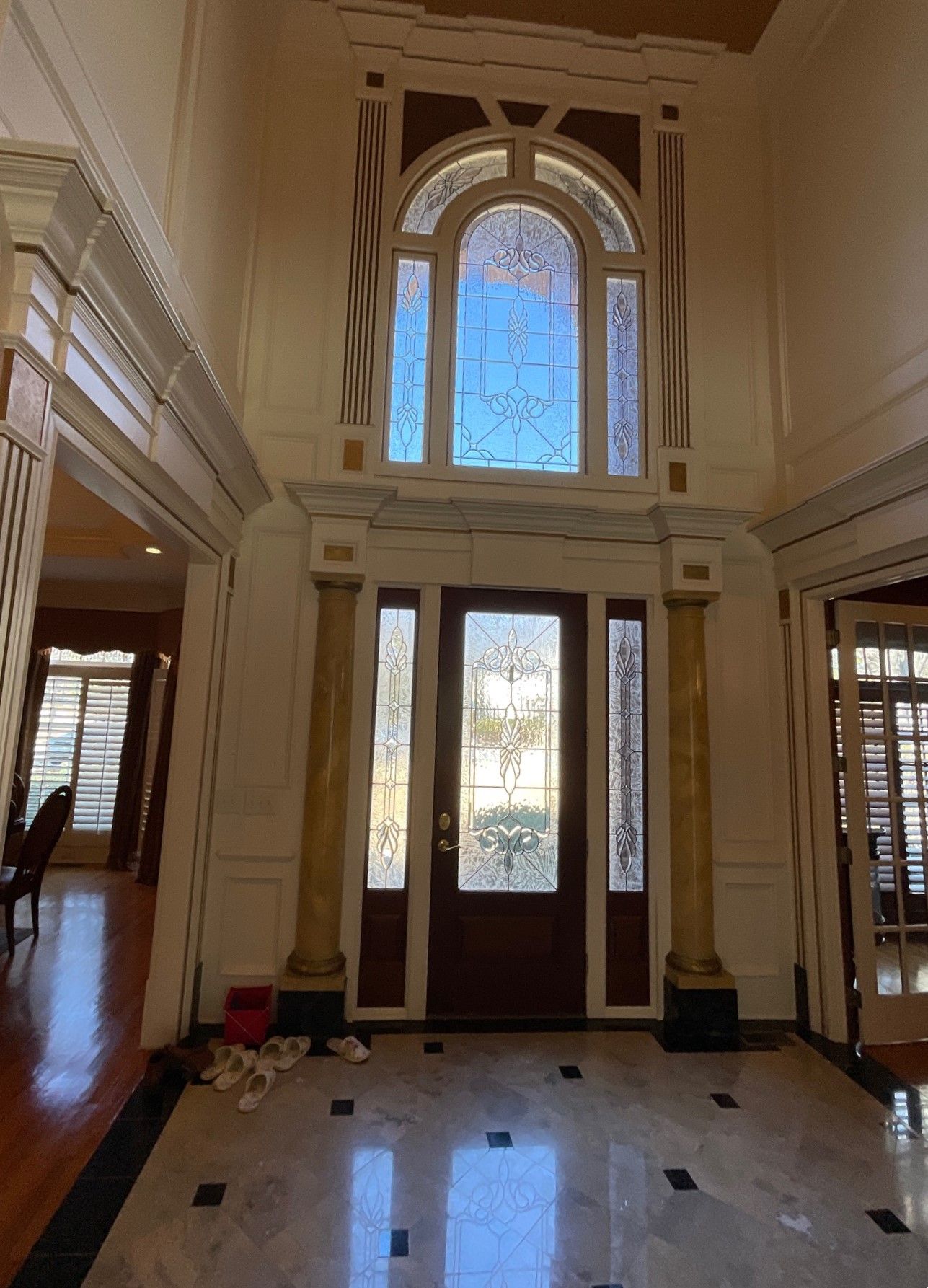 Grand foyer with a stained glass window above a dark wooden door. Marble flooring.