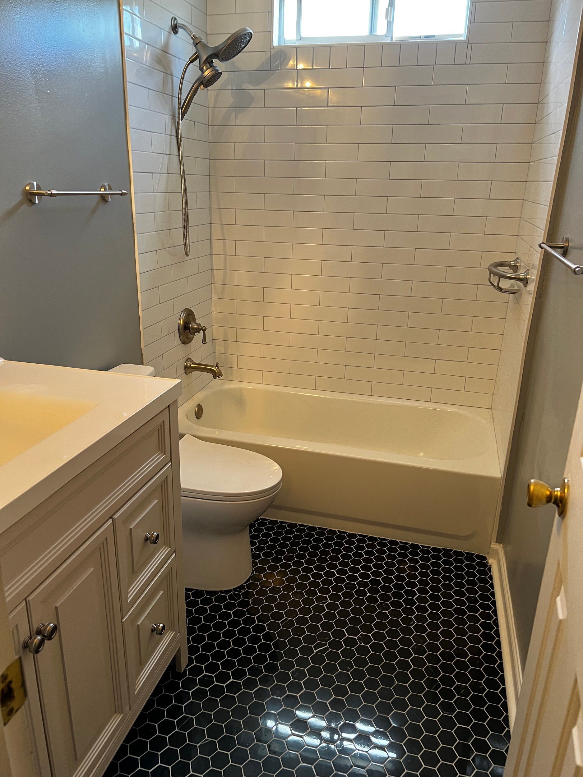 Bathroom with white vanity, toilet, bathtub with shower, and black patterned floor tiles.