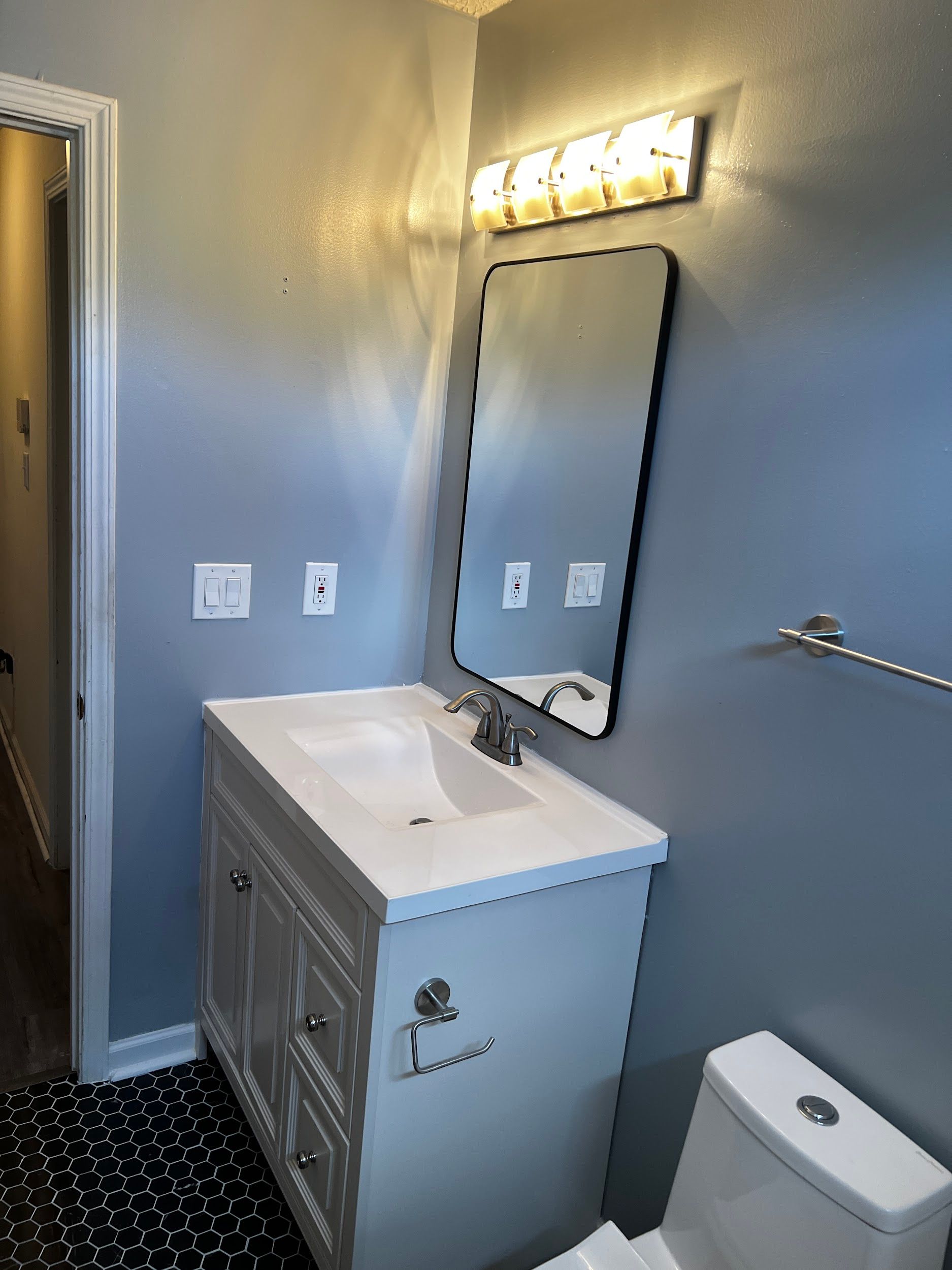 Bathroom with white vanity, black-framed mirror, and blue walls. Black and white patterned rug.