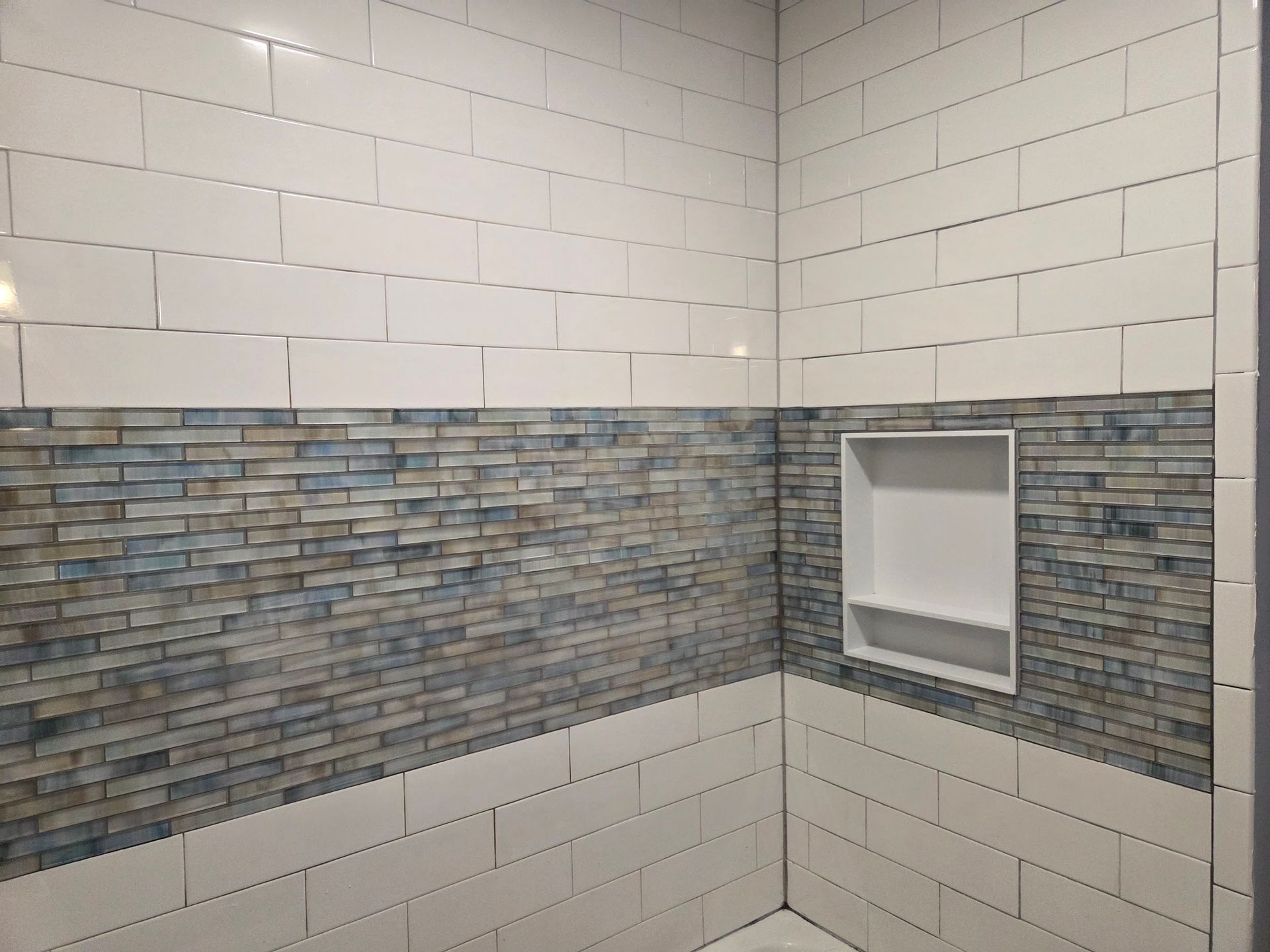 Shower with white and blue brick-patterned tile, featuring a recessed shelf.