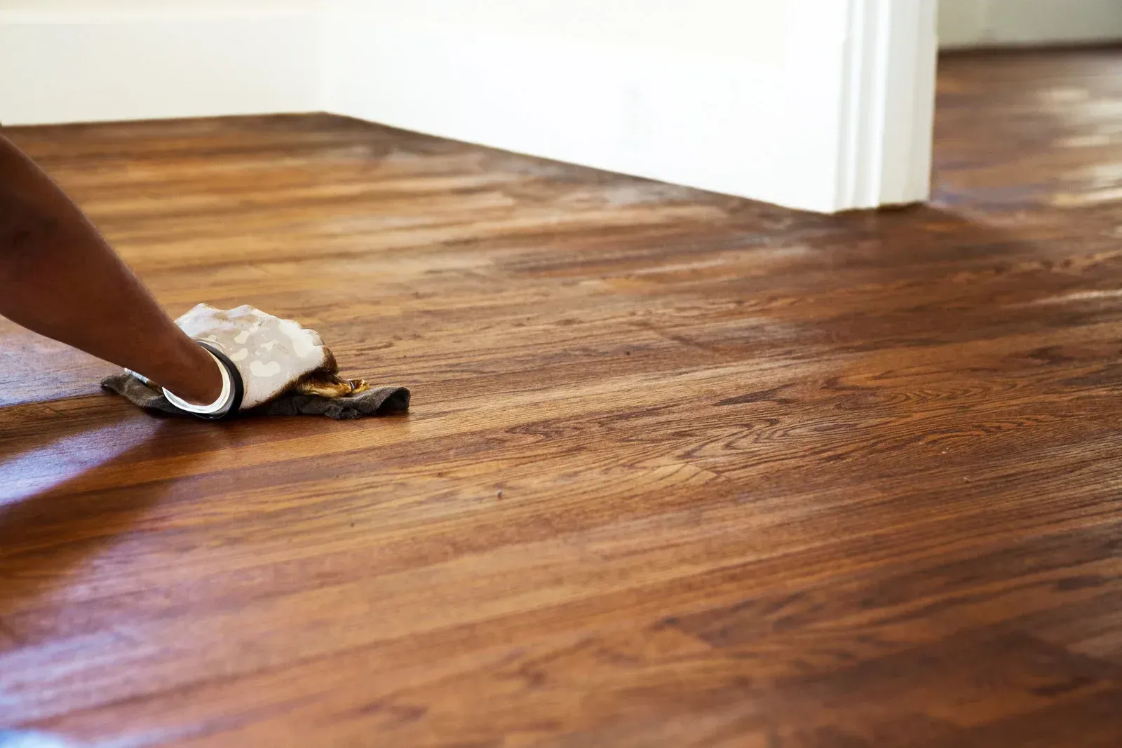 Person wiping dark stain on a wooden floor with a glove and applicator.