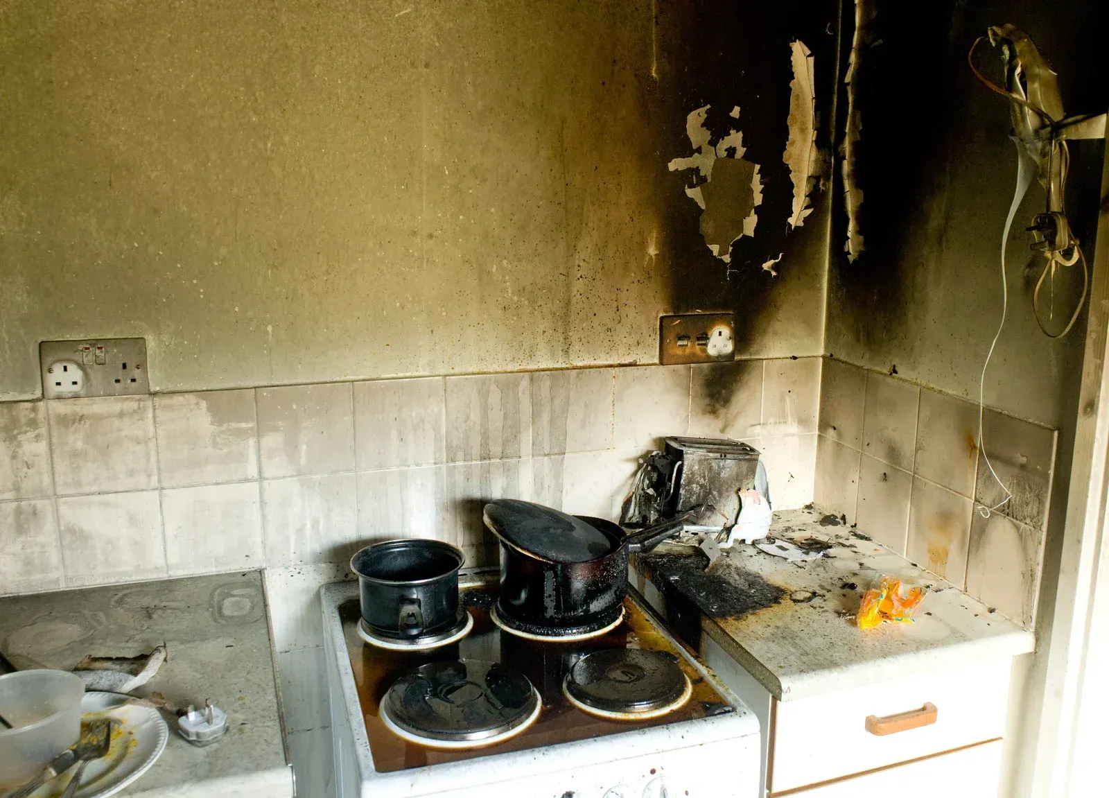 Kitchen damaged by fire. Burnt stove, pots, electrical outlets, and charred walls.