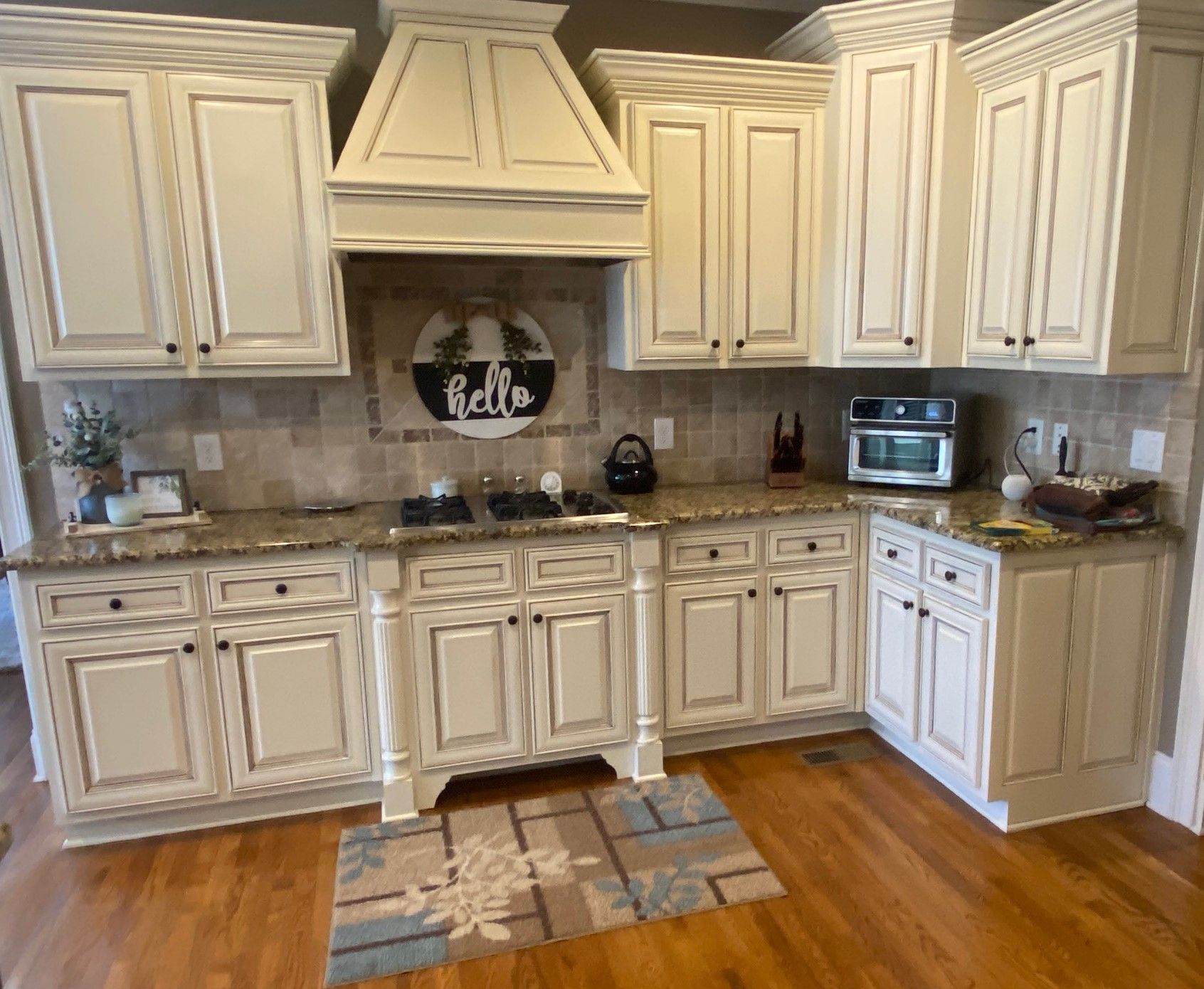 Cream-colored kitchen cabinets with granite countertops. Range hood above the stove. Wooden floor.