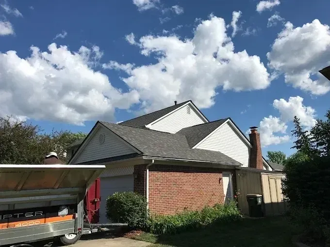 Brick house with a gabled roof and carport under a partly cloudy blue sky