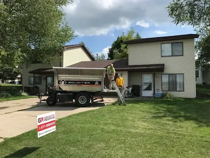 Moving truck and workers outside a house with a lawn sign in front.