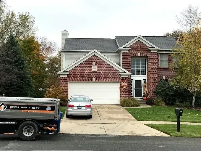 Suburban brick house with white garage, driveway, parked car, and work truck in front